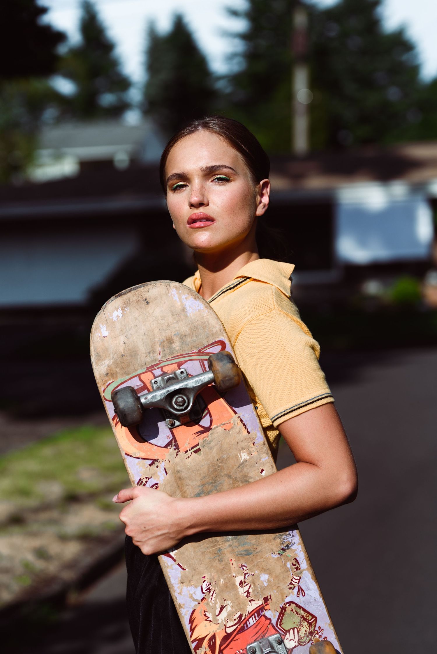 Portrait of person holding vintage skateboard wearing yellow polo shirt outdoors.