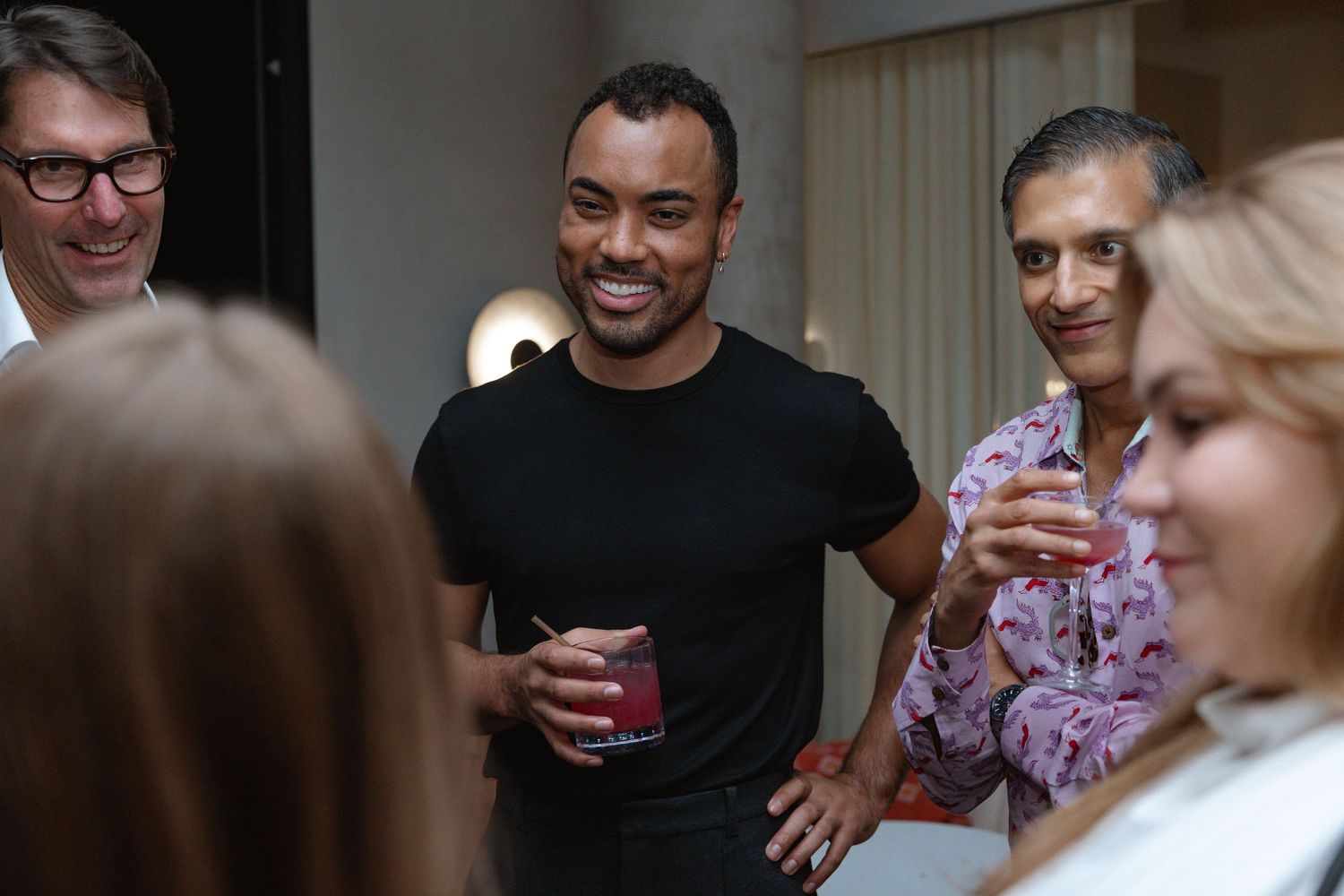 A group of people enjoying drinks and conversation at a social gathering indoors.