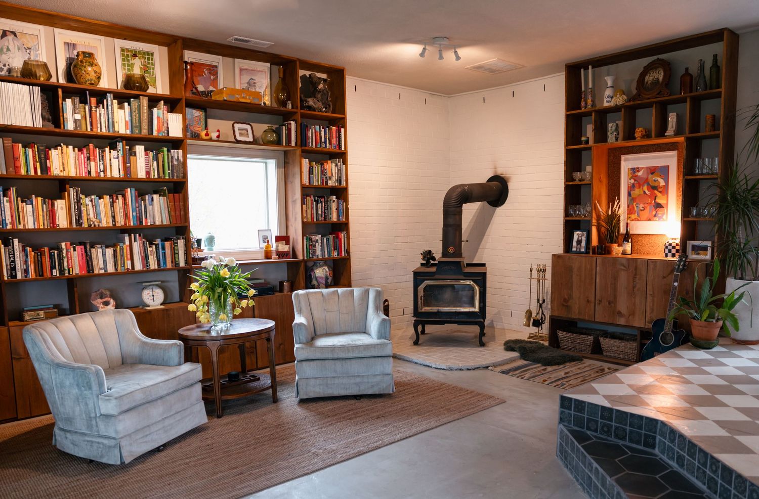 Cozy library room with floor-to-ceiling bookshelves, blue armchairs, and wood burning stove.