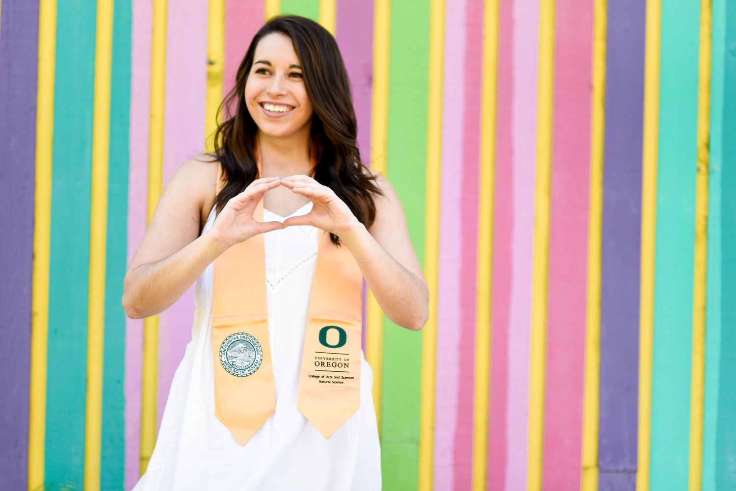 Graduate with Oregon sash against colorful striped wall background.