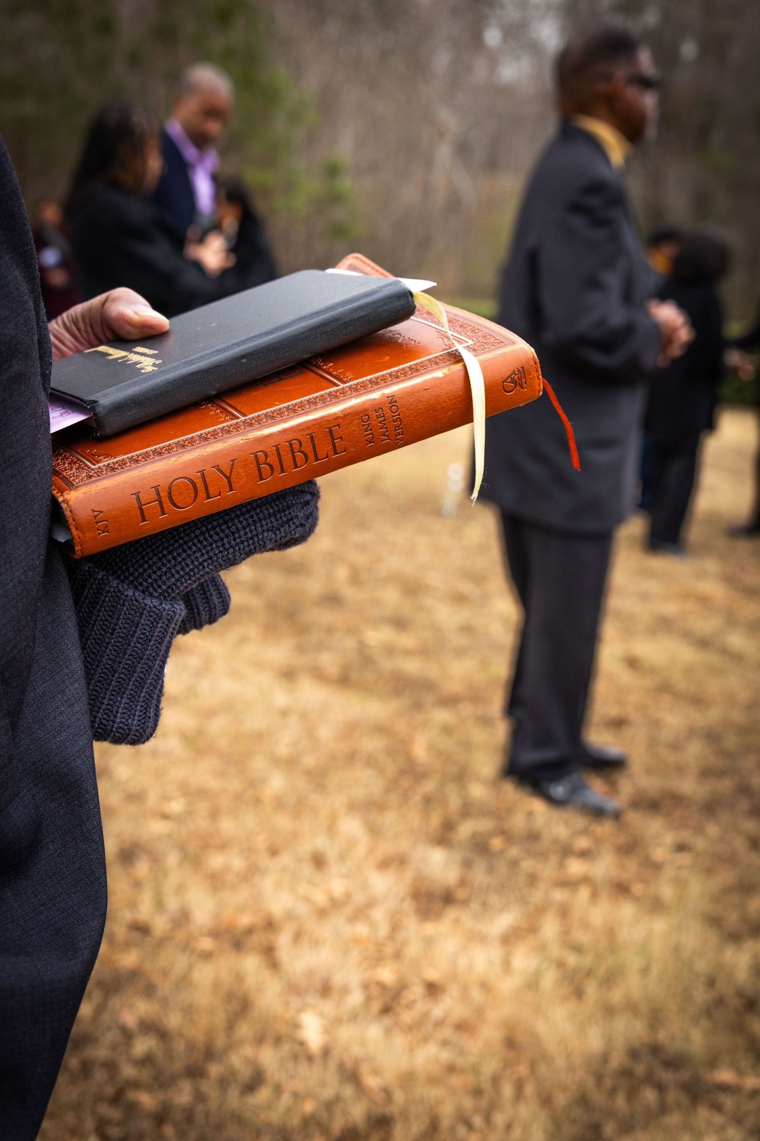 A leather-bound Holy Bible being held in gloved hands during an outdoor ceremony.