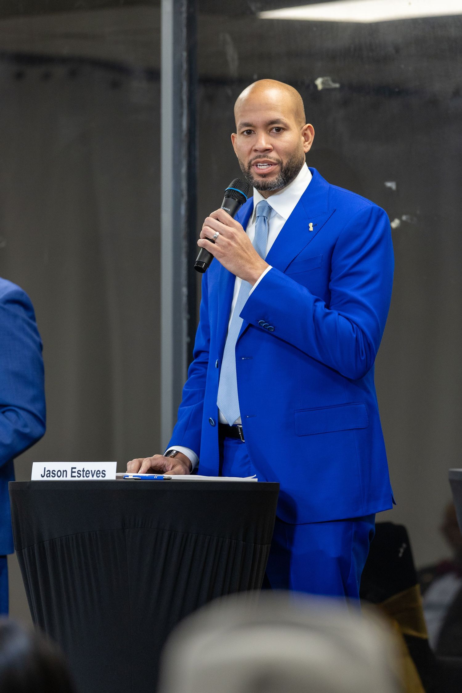 A speaker in a bright blue suit jacket addresses an audience from behind a podium during a formal event.