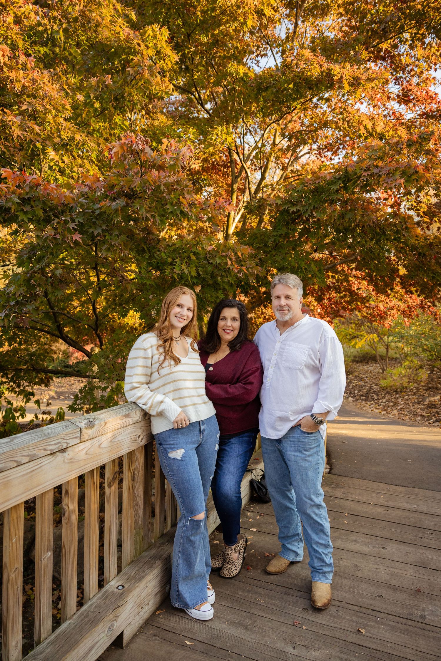 Family photo session on wooden deck with golden fall foliage in background.