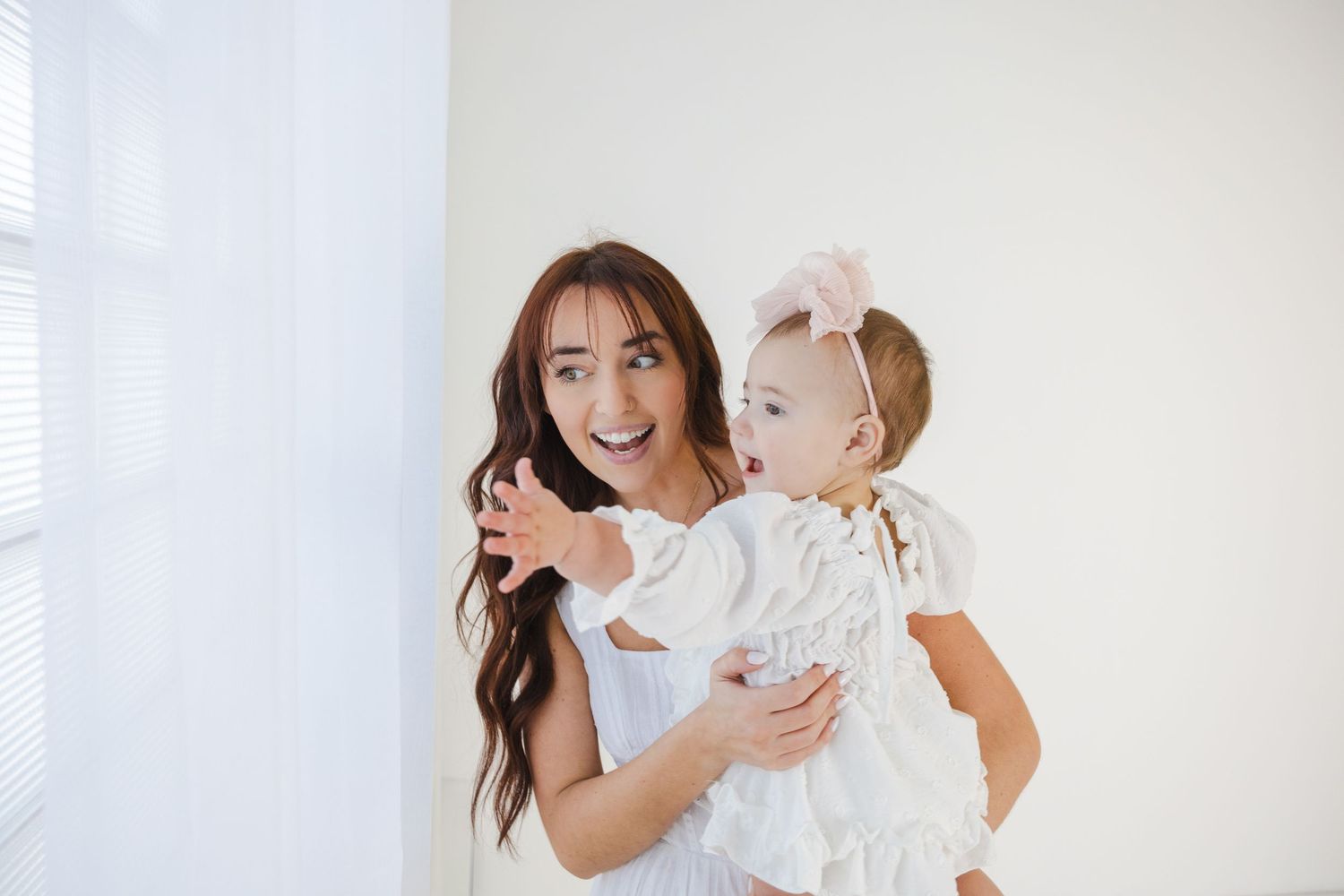 Joyful studio portrait with mother and baby in white attire.