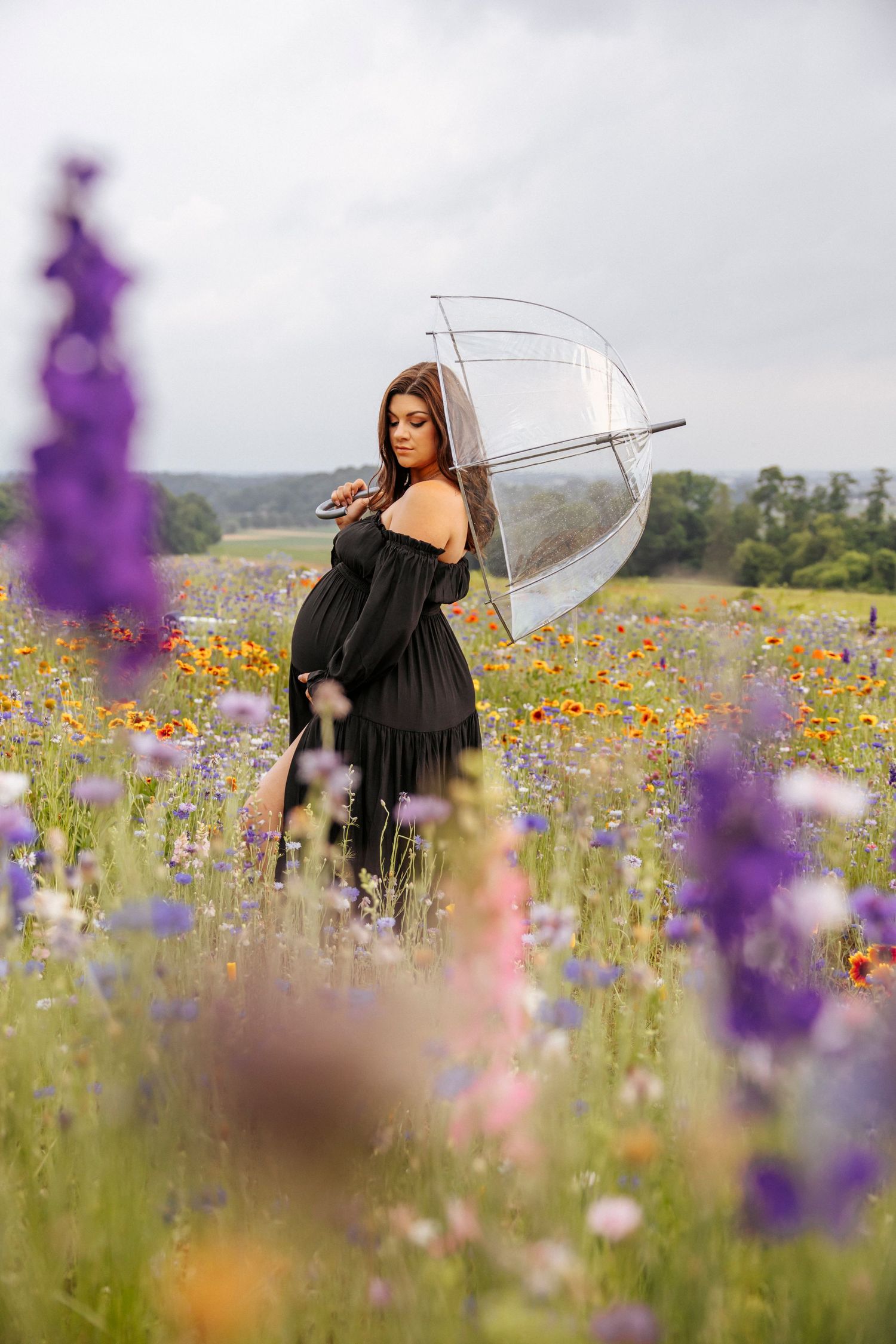 Person in black dress with umbrella stands among colorful wildflowers on an overcast day.