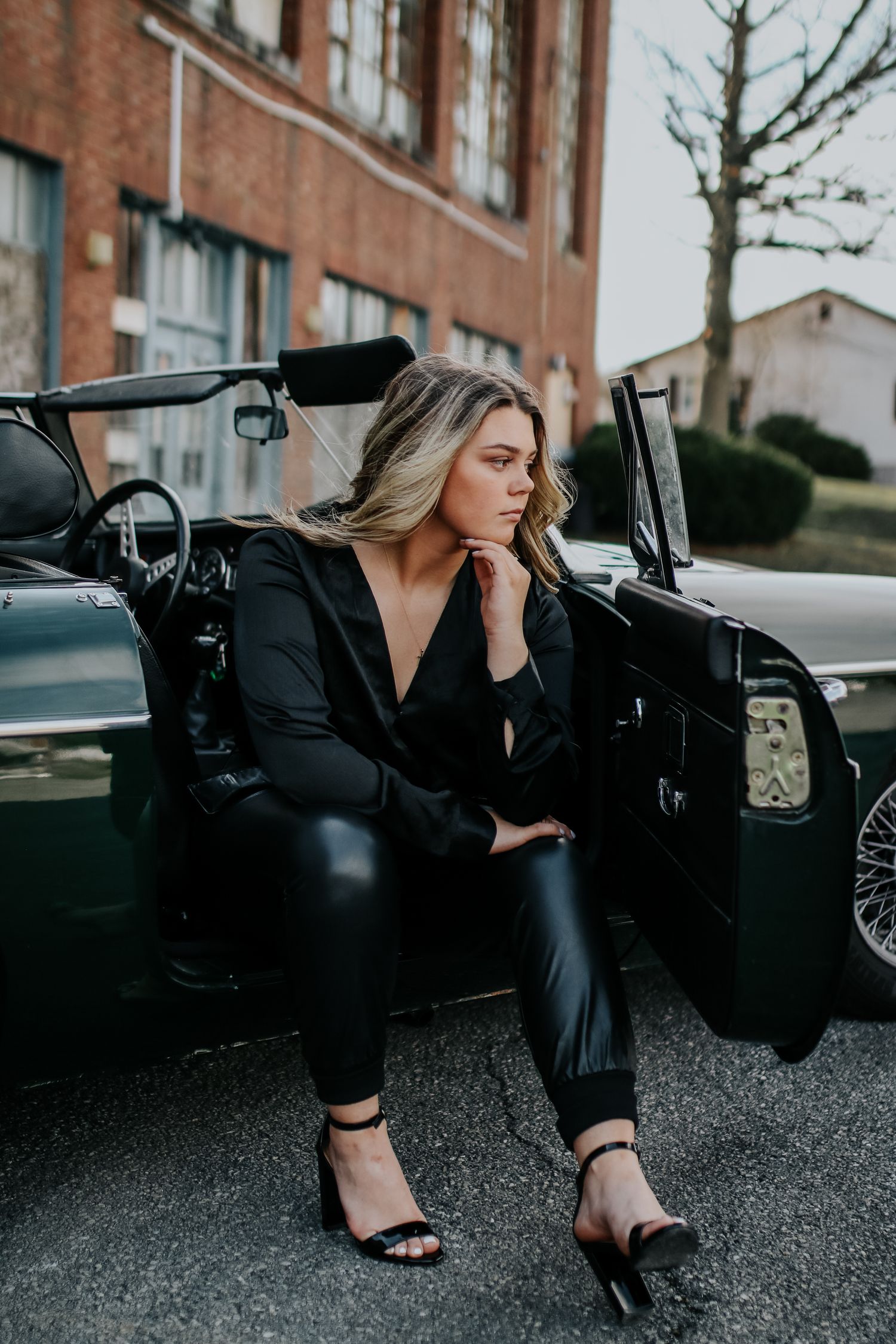Moody portrait session with vintage car on gravel parking lot.