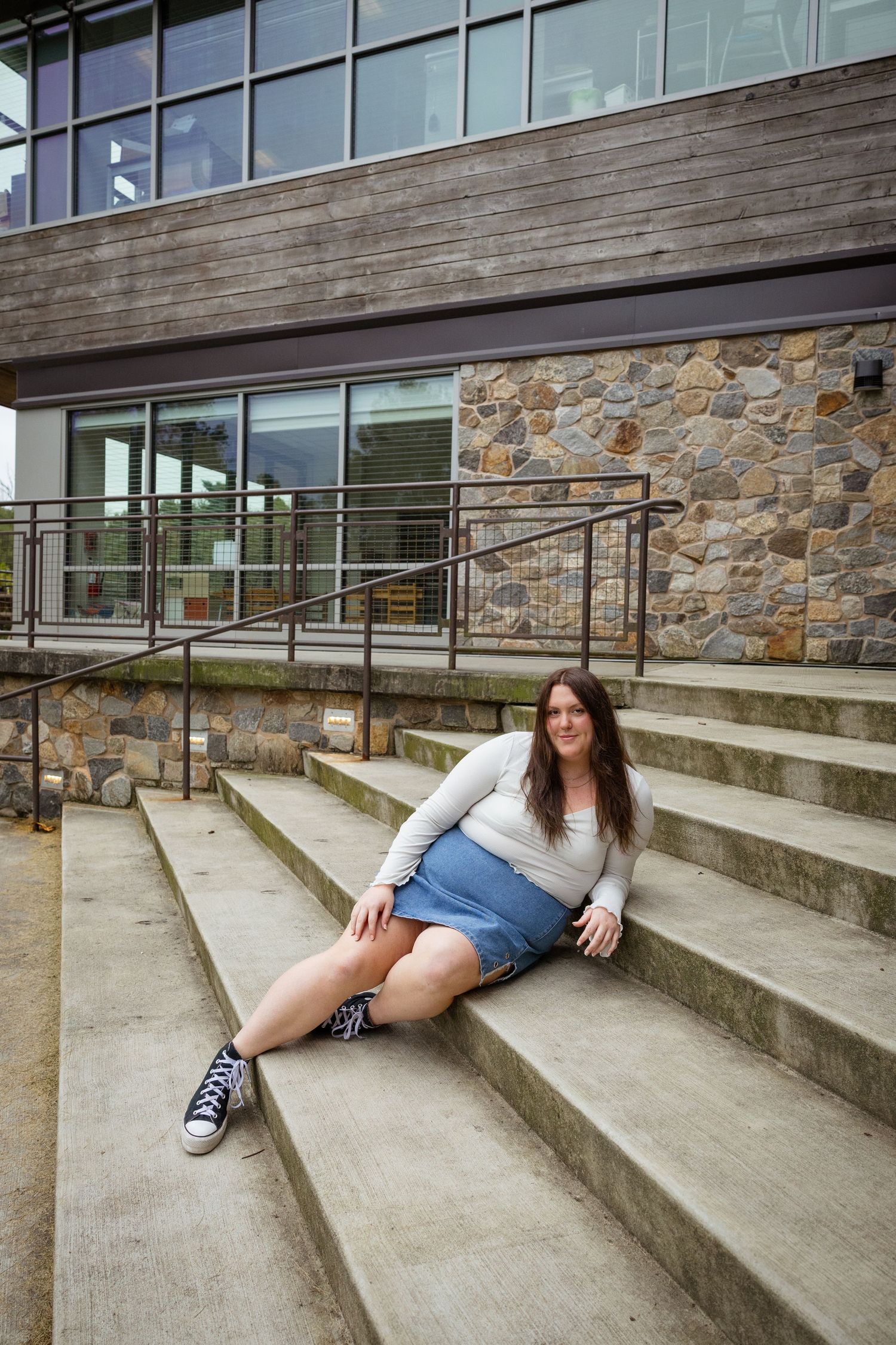 Person in white top and denim sitting casually on concrete steps with stone and wood building facade.