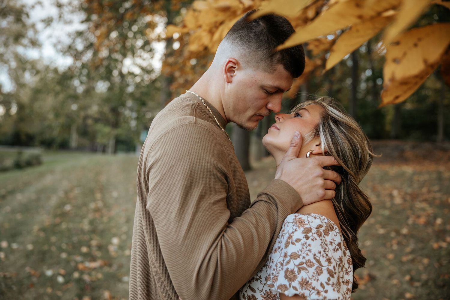 Romantic couple embraces under golden autumn leaves in outdoor photoshoot.