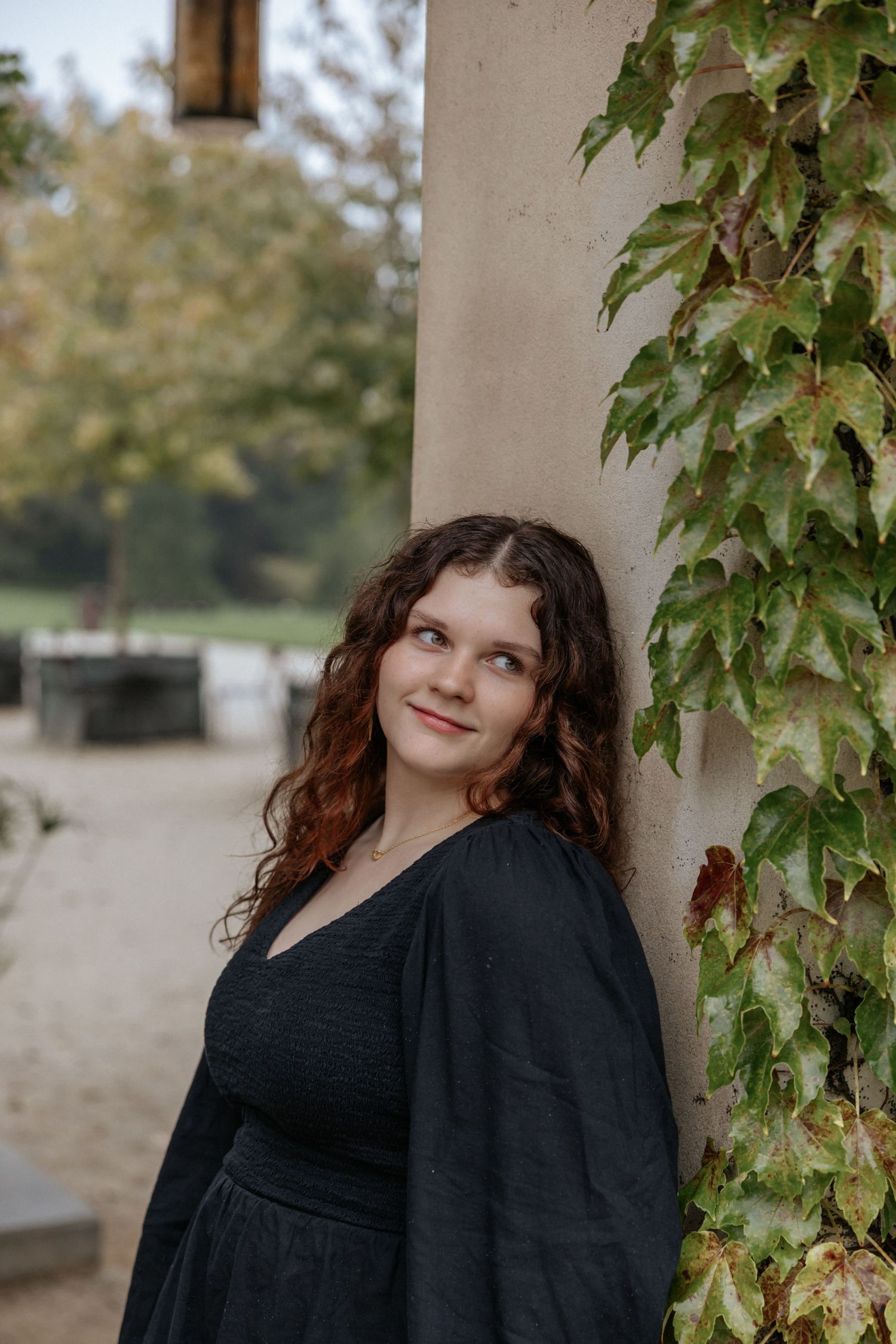 An autumn portrait against ivy-covered architecture wearing a black dress and cardigan.