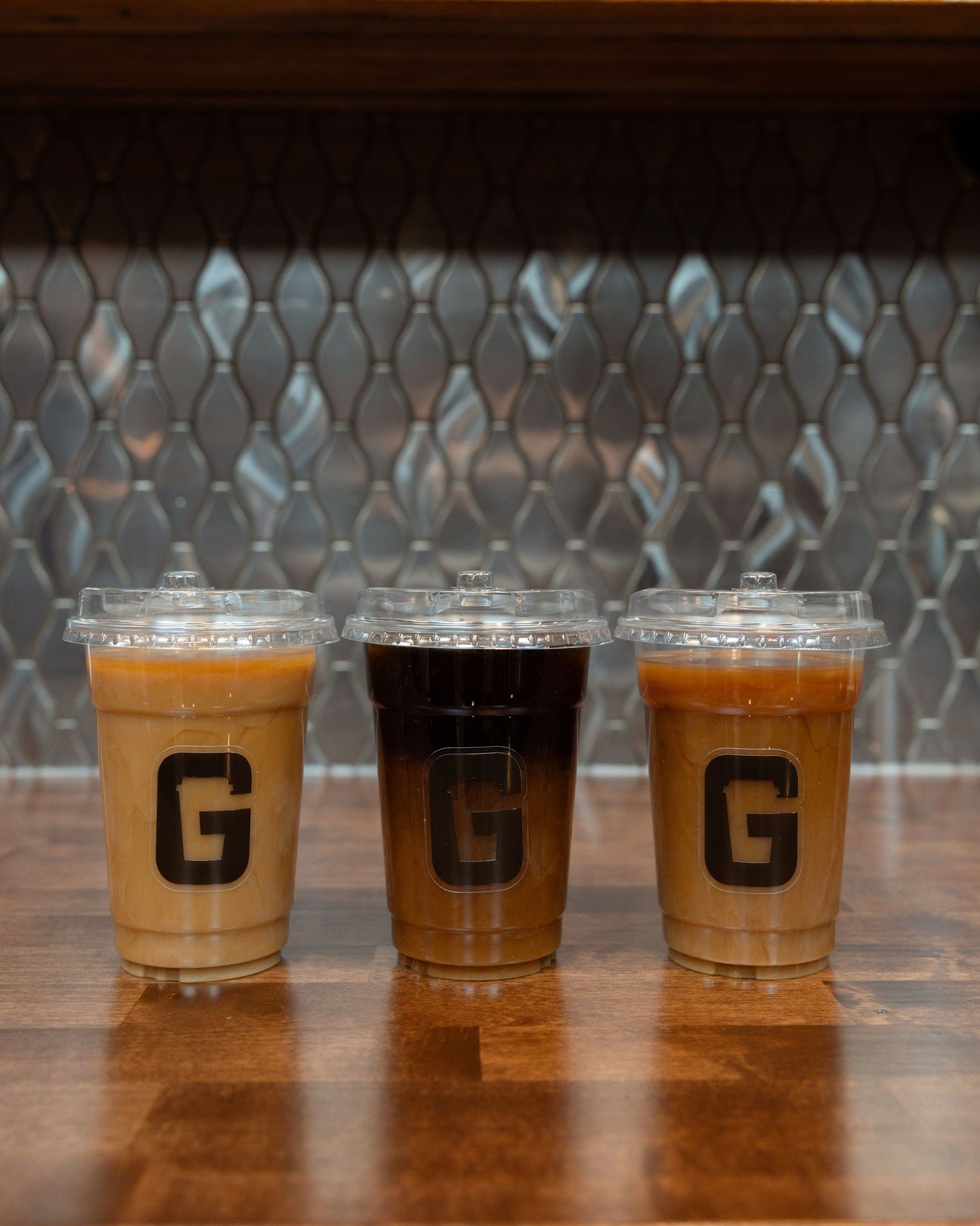 Row of clear plastic cups with different colored beverages on a wooden table.