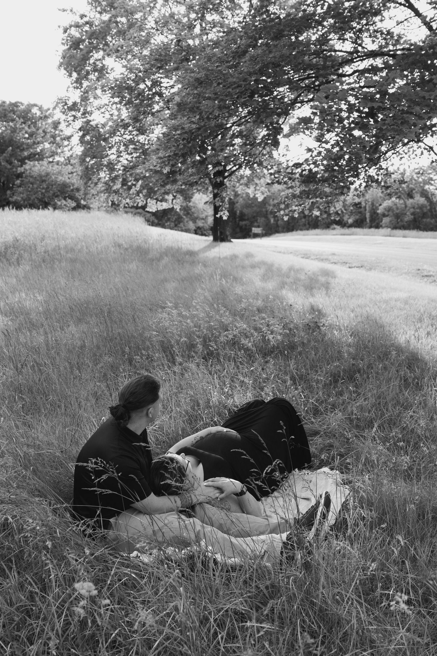 Black and white photo of couple resting together in meadow.