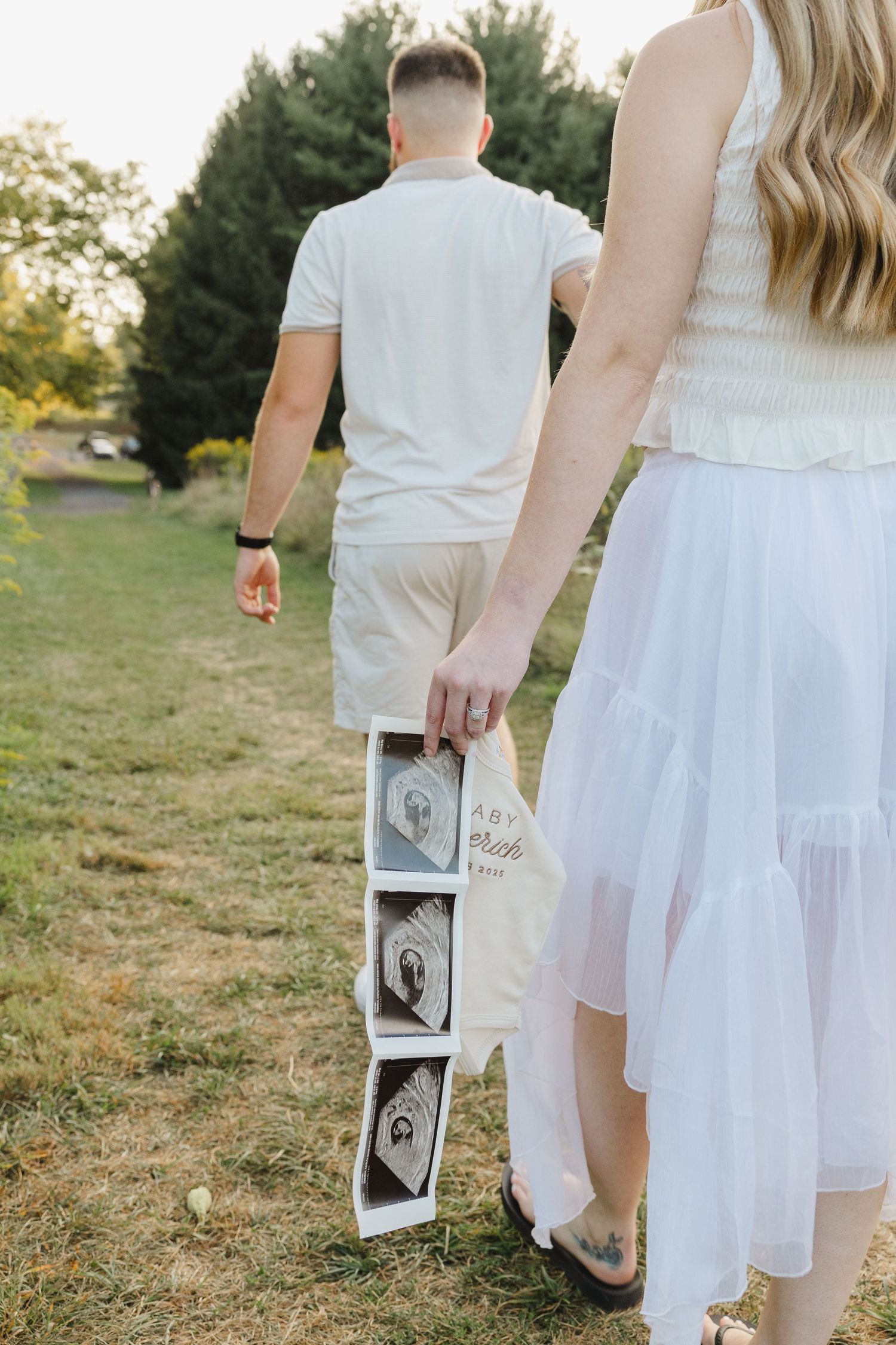 Side view of couple walking through a field holding ultrasound pictures.