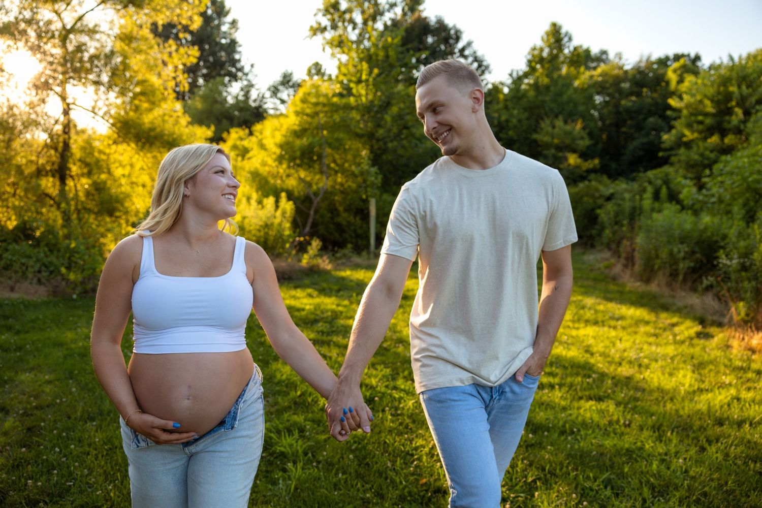 Couple in casual wear poses for maternity photos in a sun-drenched field.