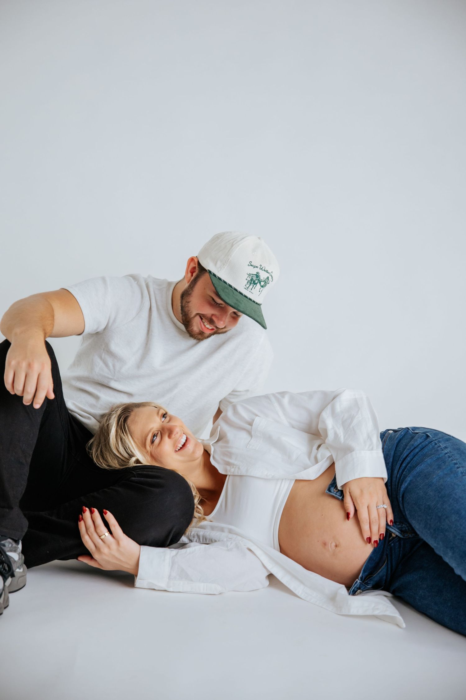 Artistic maternity photo with couple laying down on white background.