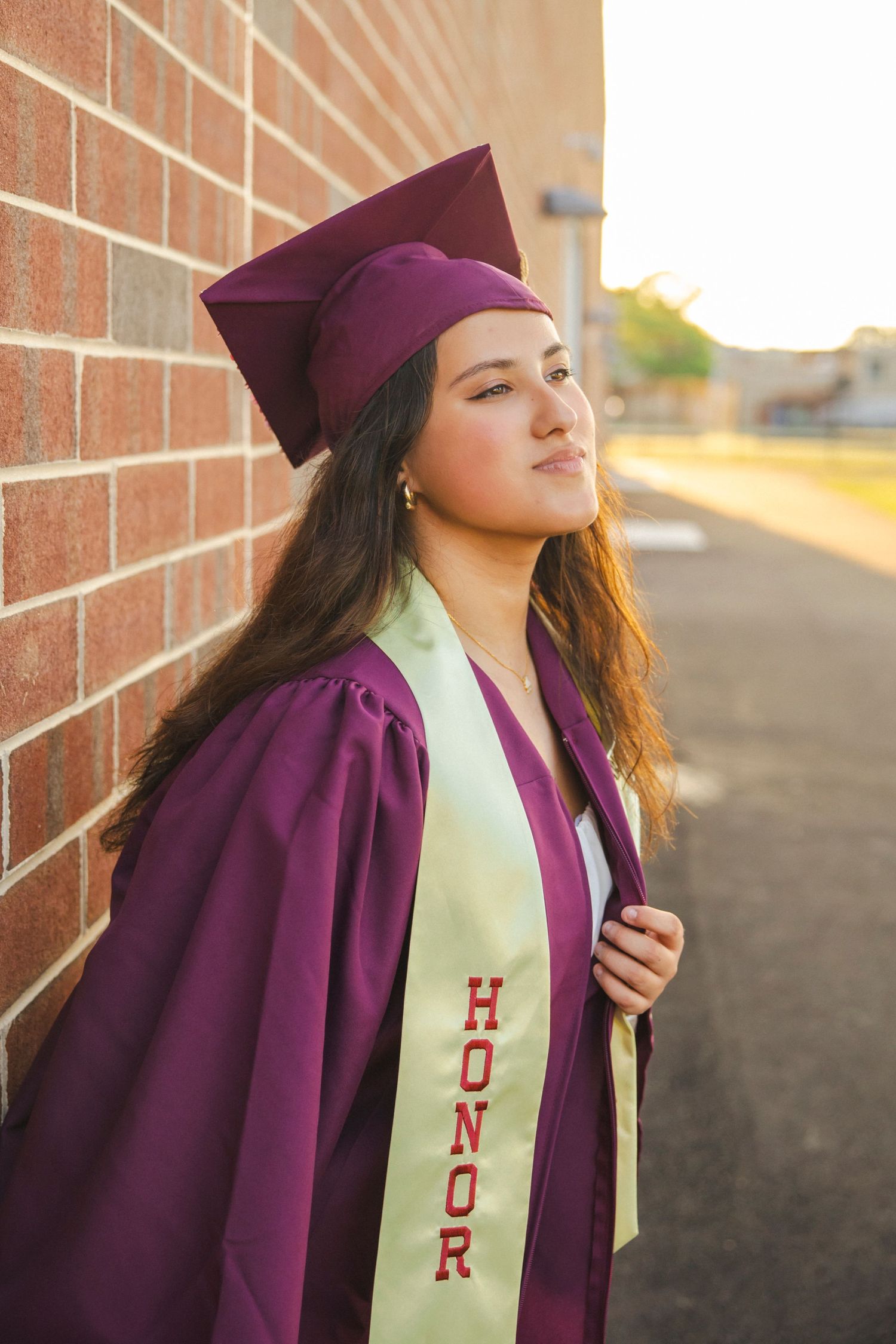 Graduate wearing purple cap and gown with honor stole poses for portraits.