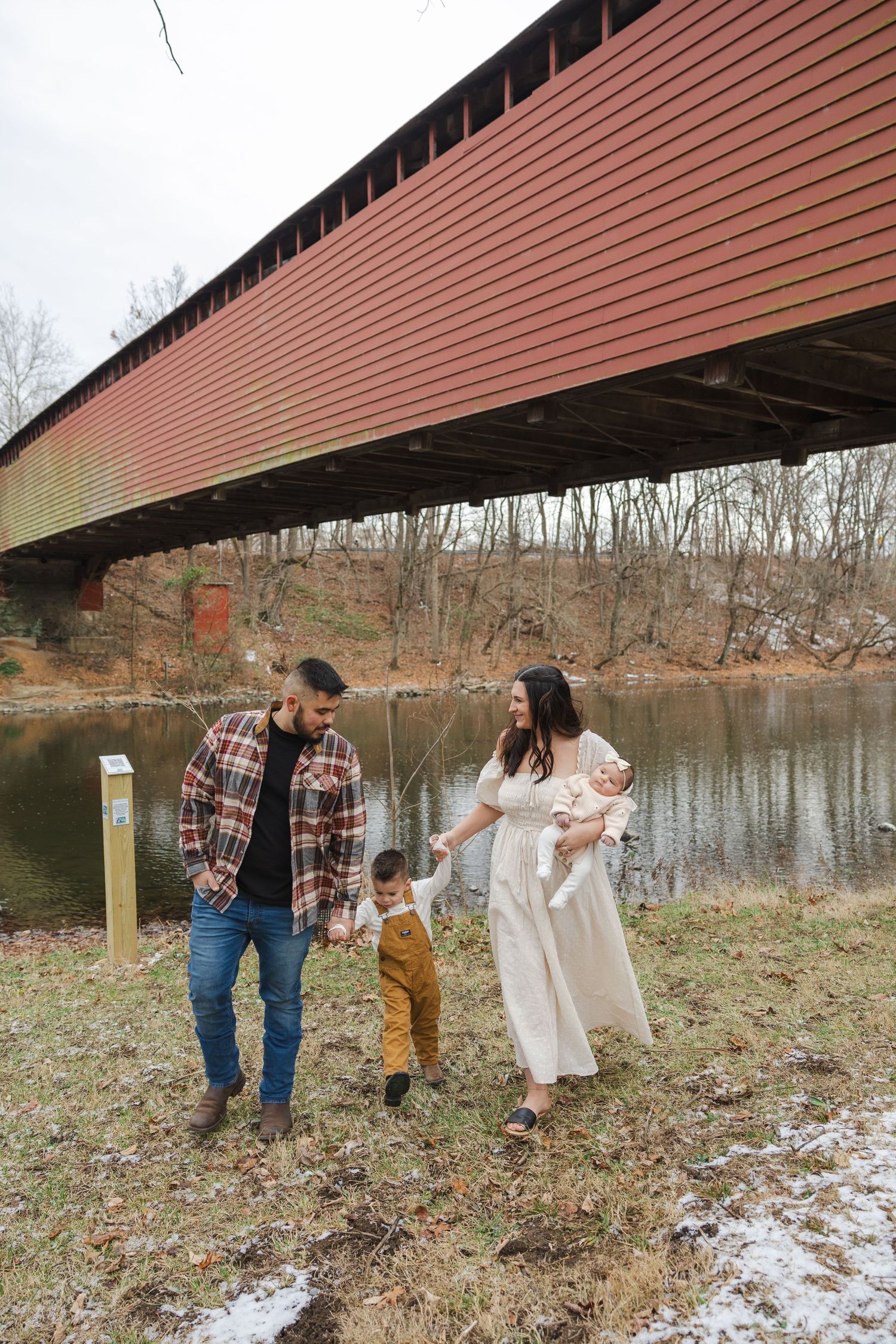 Family walking together near red covered bridge on autumn day.