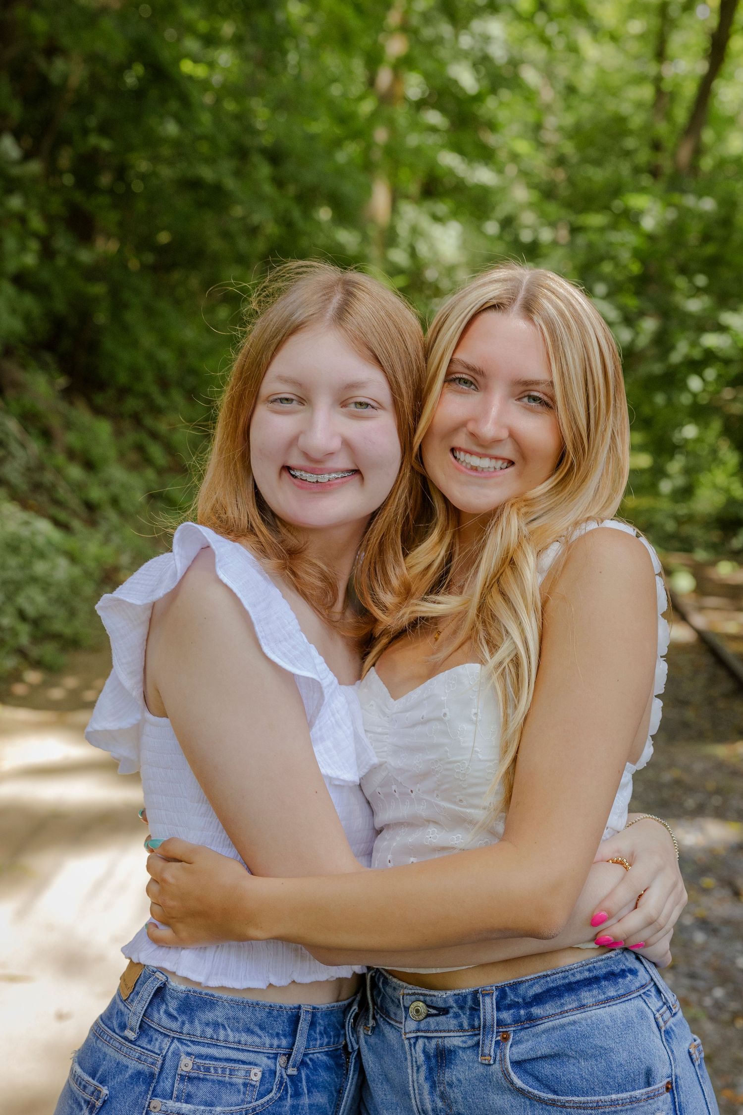 Two friends embrace and smile warmly at each other in a natural outdoor setting.