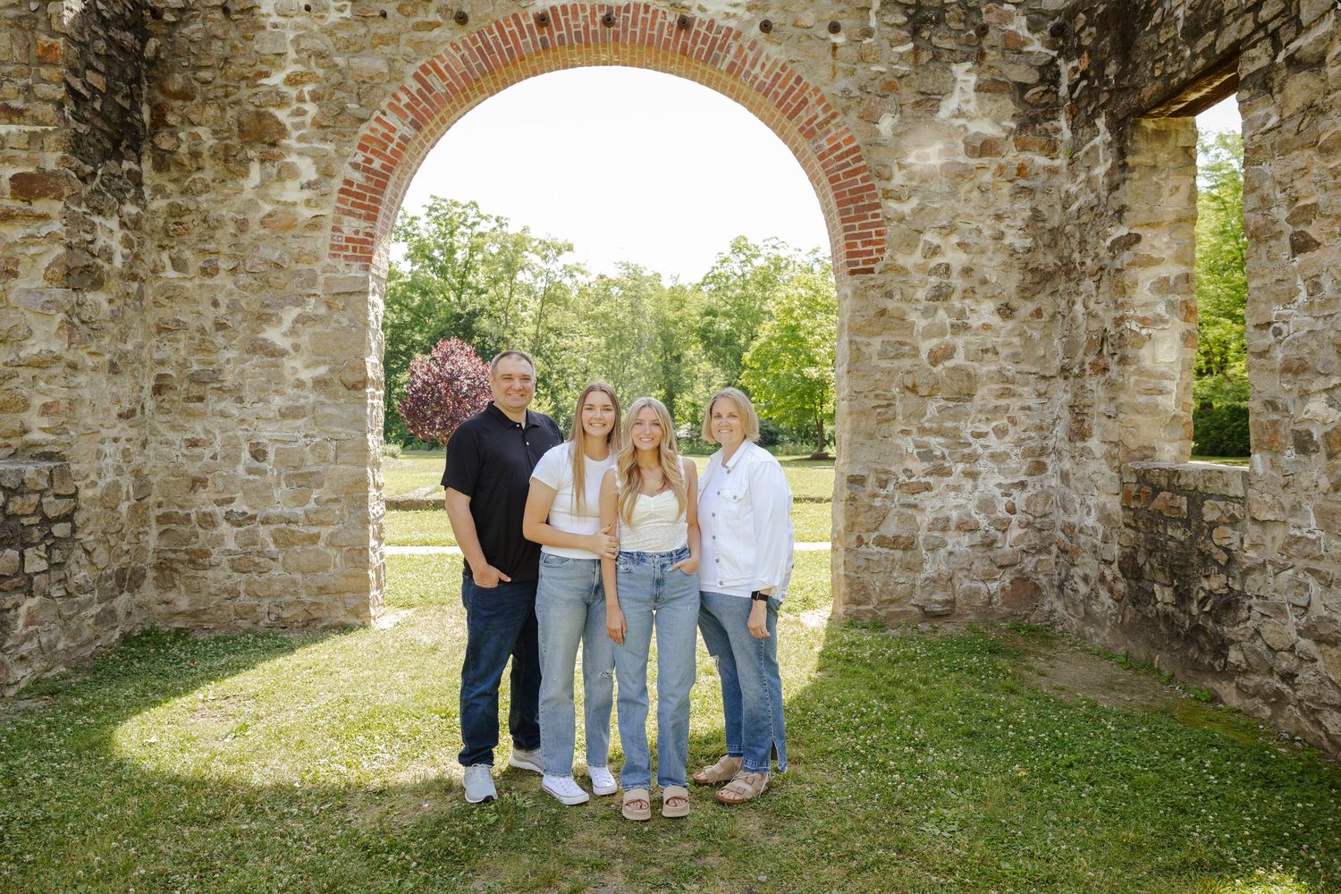 Family portrait session at rustic stone arch location in coordinated casual outfits.