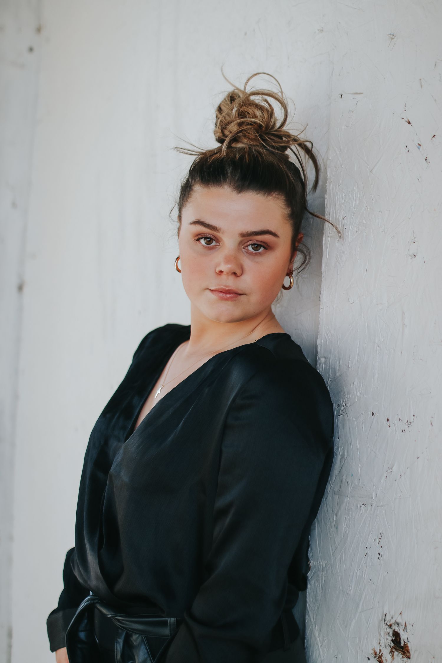 Artistic portrait series against white wall featuring black wrap dress and casual styling.