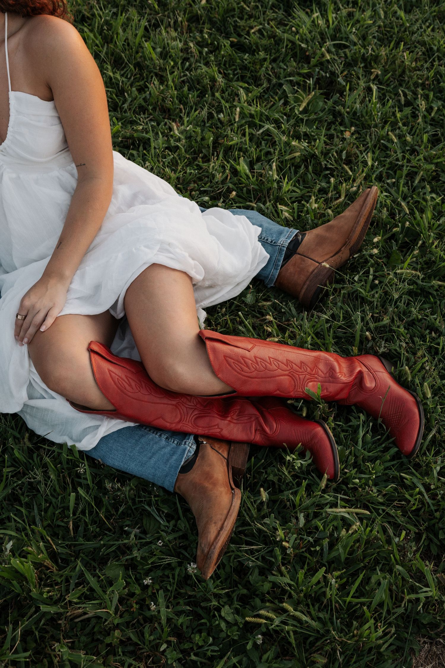 Person relaxing on grass wearing white dress and red cowboy boots.