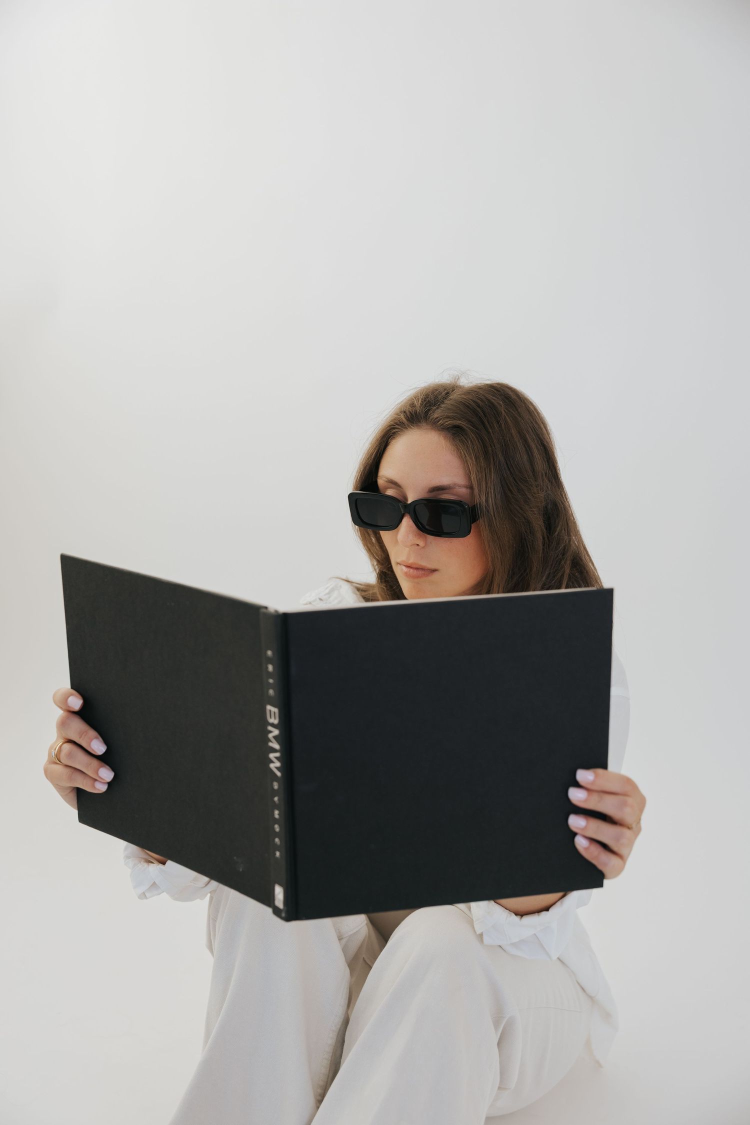 Creative poses with person reading large black book wearing sunglasses and white shirt.