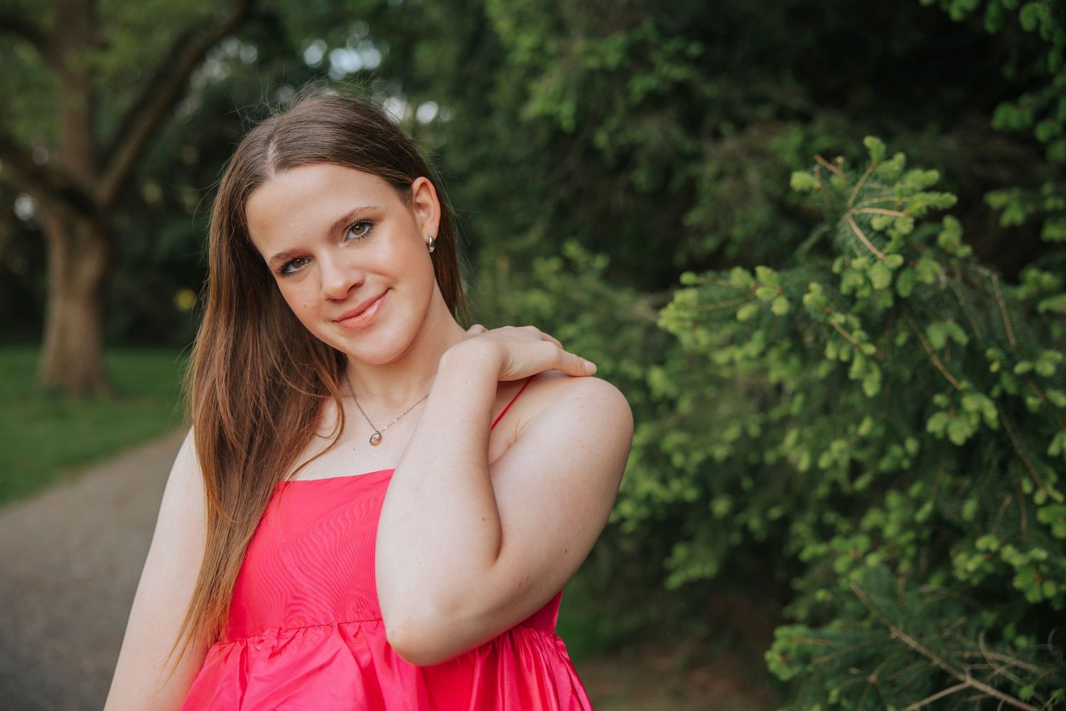 Portrait of person in bright coral dress posing against green foliage background.