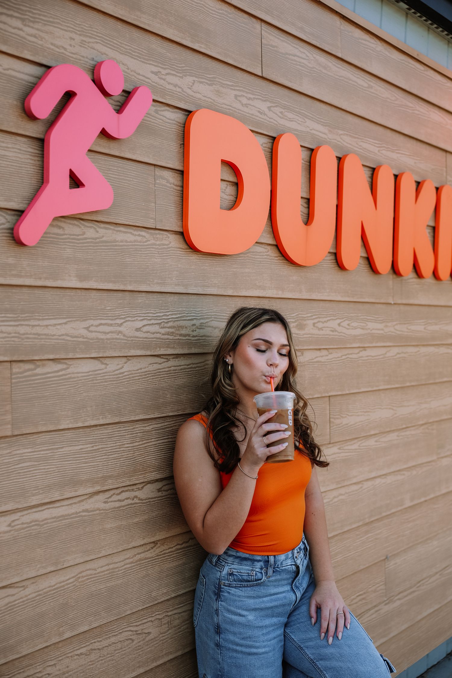 Orange and pink Dunkin' signage mounted on wooden wall exterior.