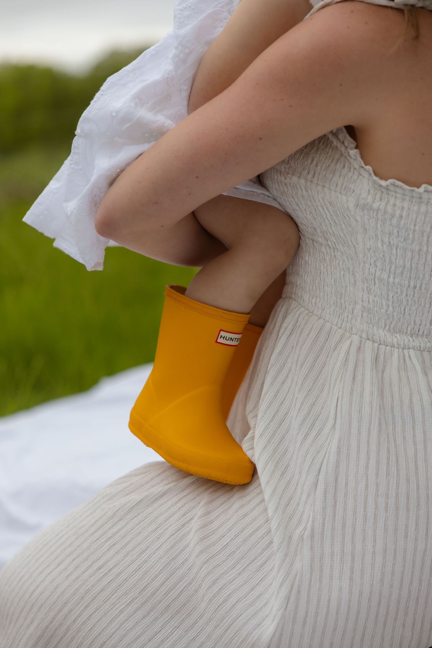 Close-up detail of a white smocked dress and yellow accessory against a natural background.