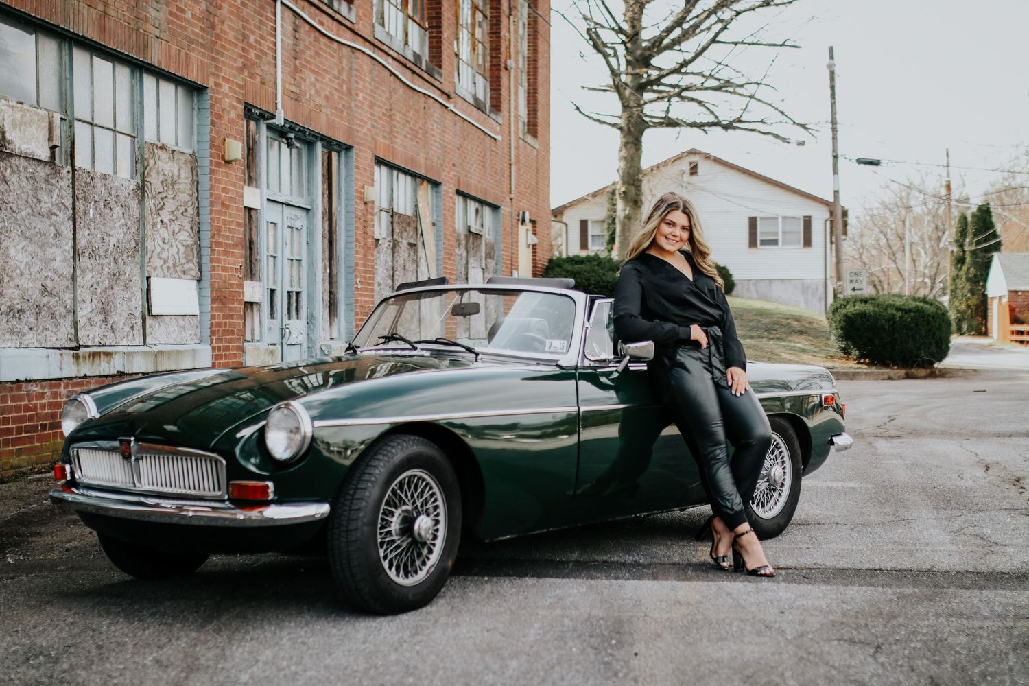A vintage dark green sports car parked against a brick building backdrop.