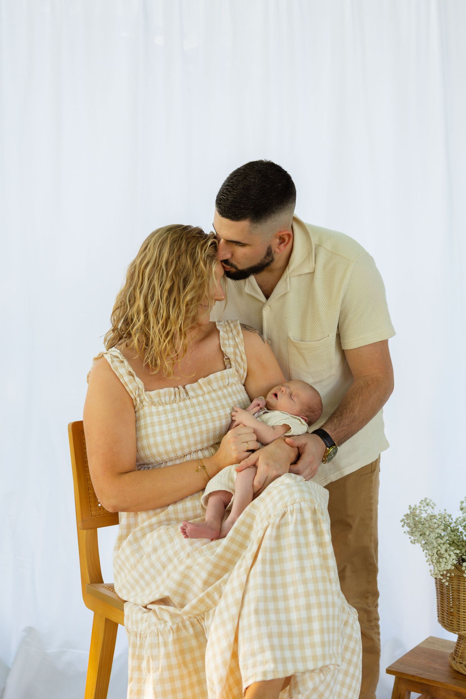 Parents sharing tender moments with their newborn baby while seated on wooden chair.