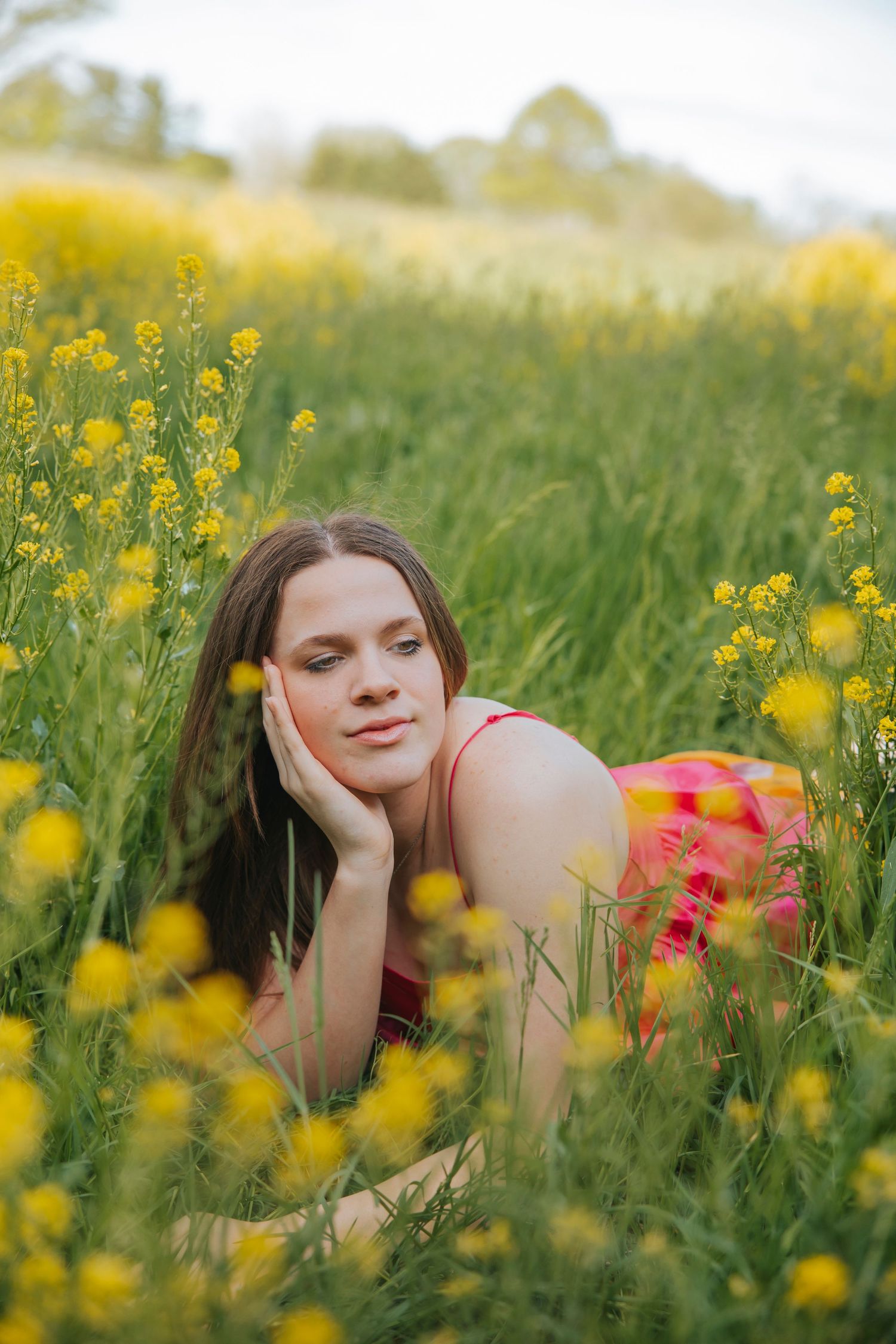 Person in coral dress lying among yellow wildflowers in sunny meadow.