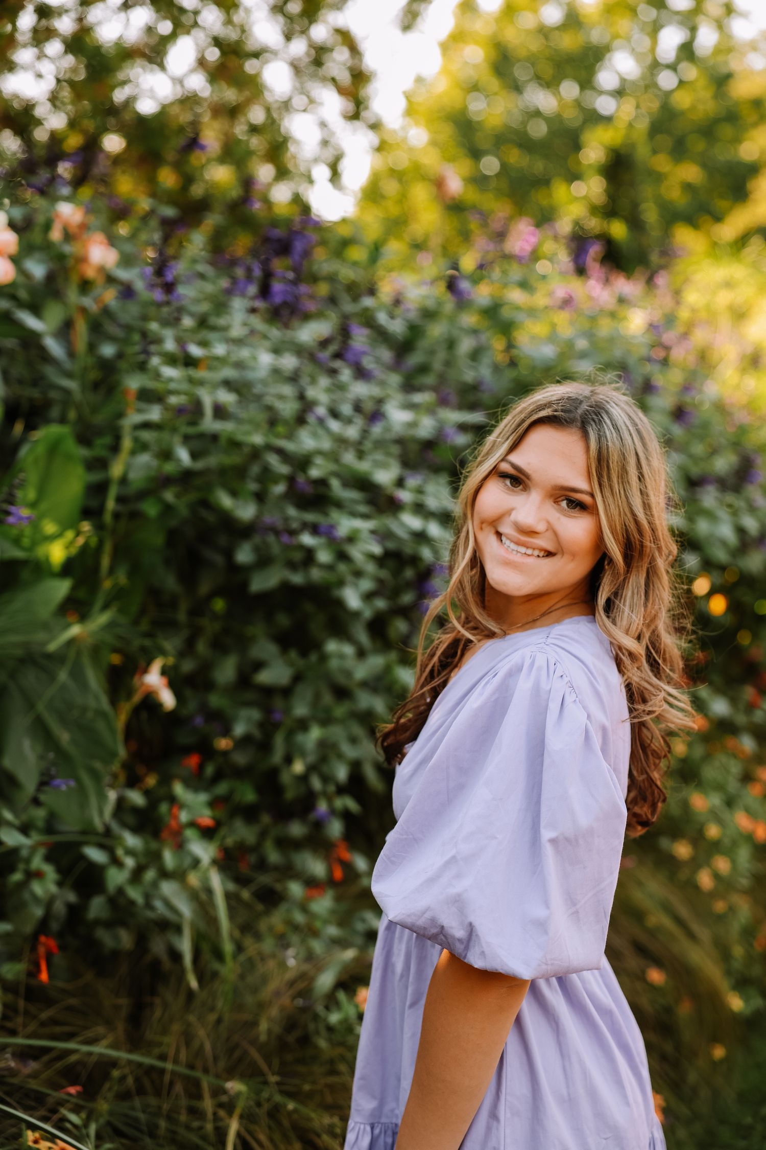 Joyful outdoor portraits in a light purple dress surrounded by summer greenery.