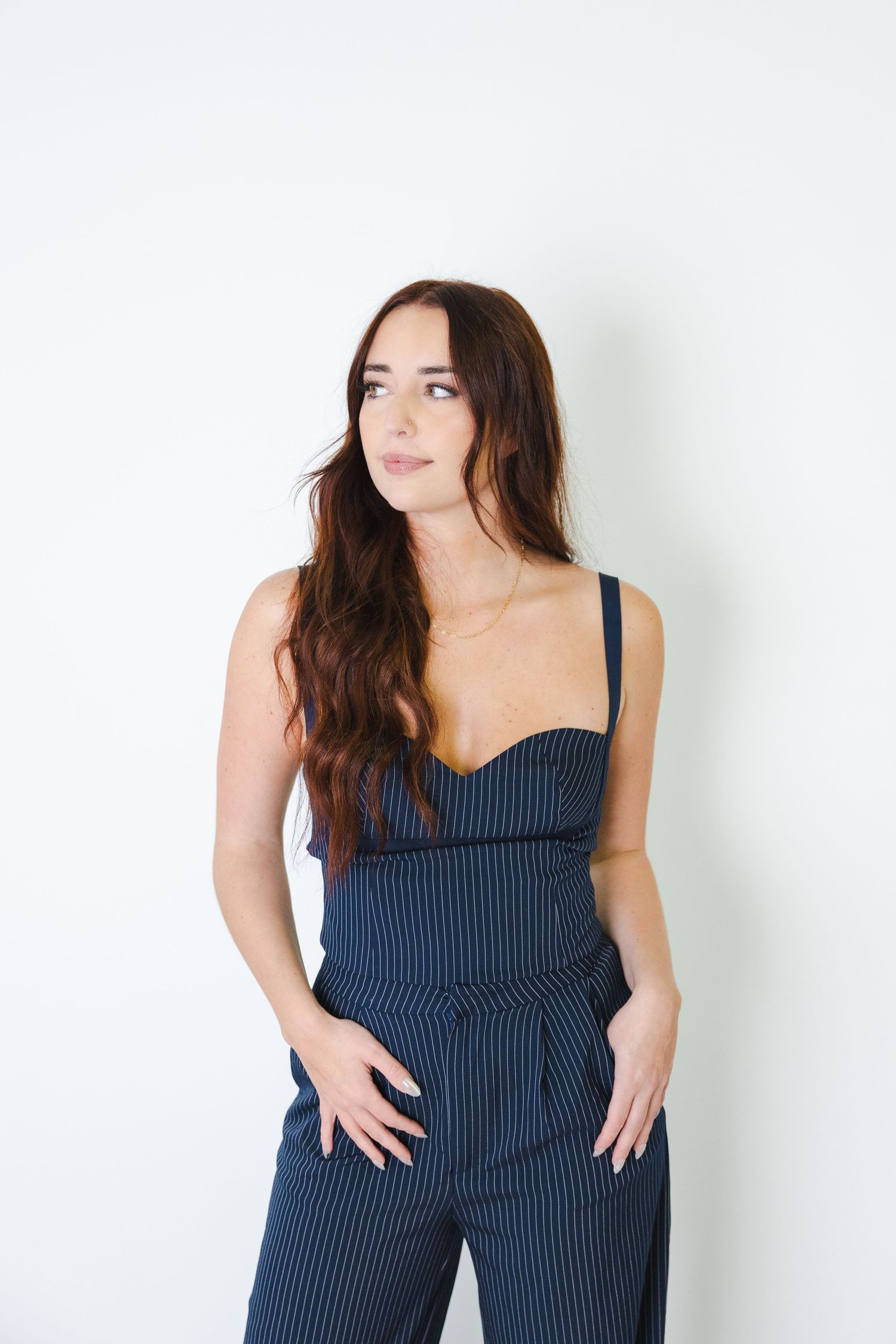 Person wearing navy pinstripe jumpsuit poses casually against white studio wall.
