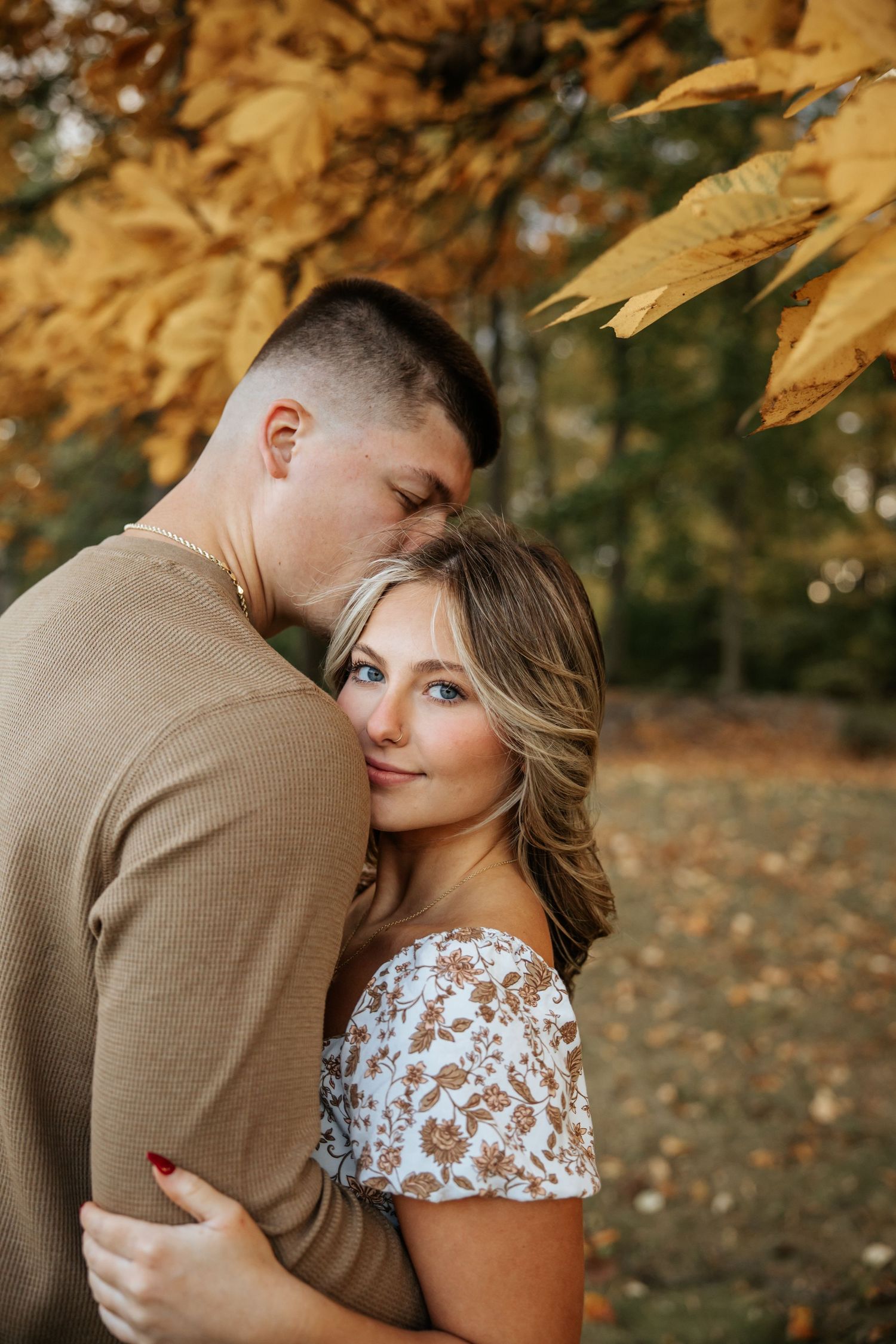 Intimate couple moment captured beneath fall foliage in warm natural lighting.