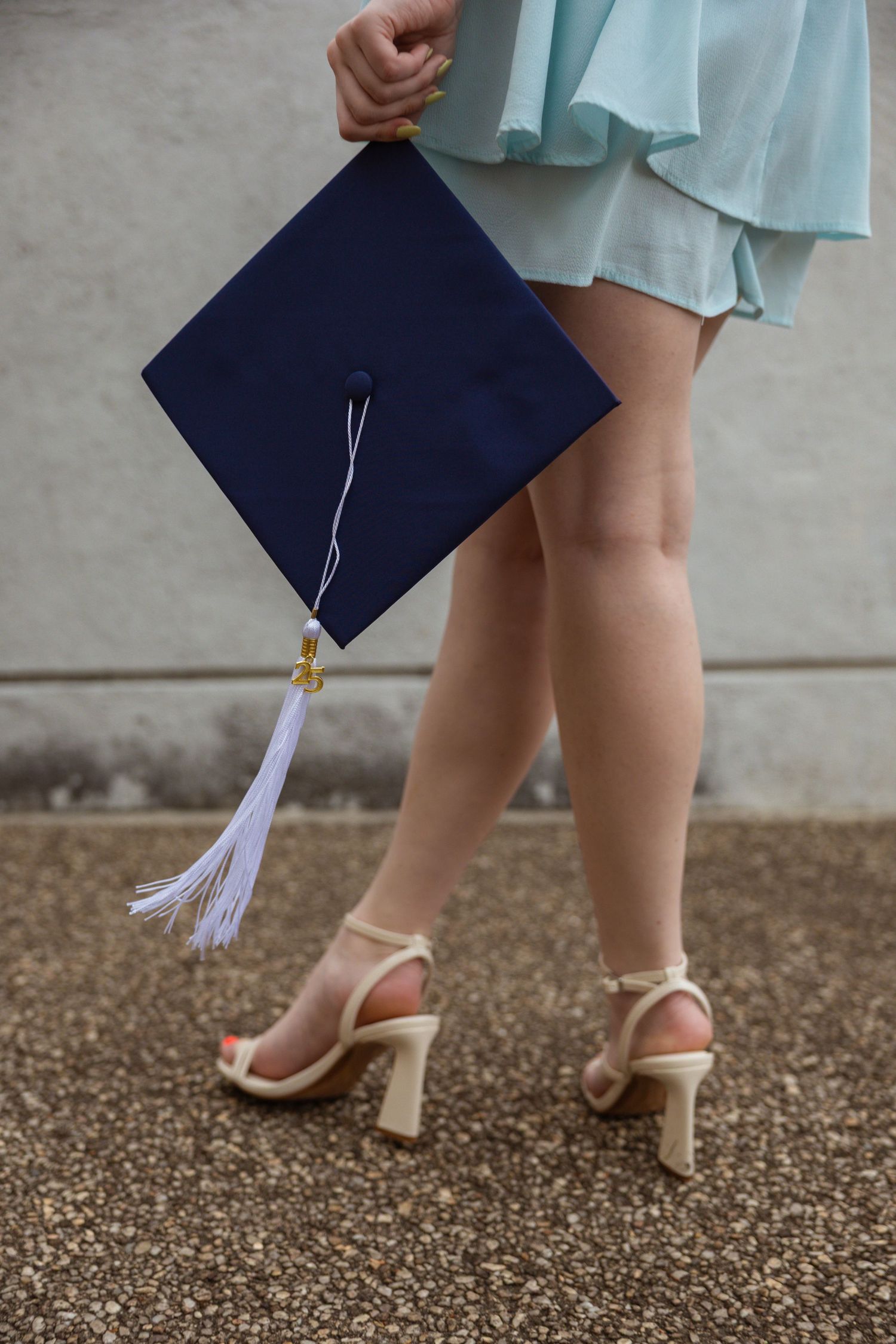 Close-up shots of graduation cap and heels against textured ground during a photo session.