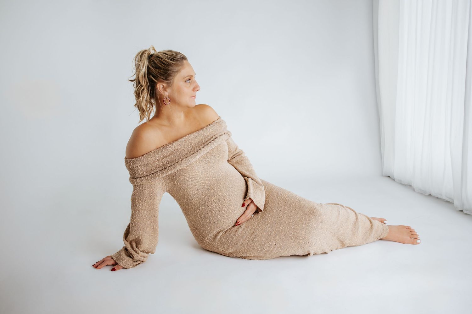 Elegant maternity poses captured with someone wearing a beige off-shoulder sweater dress.