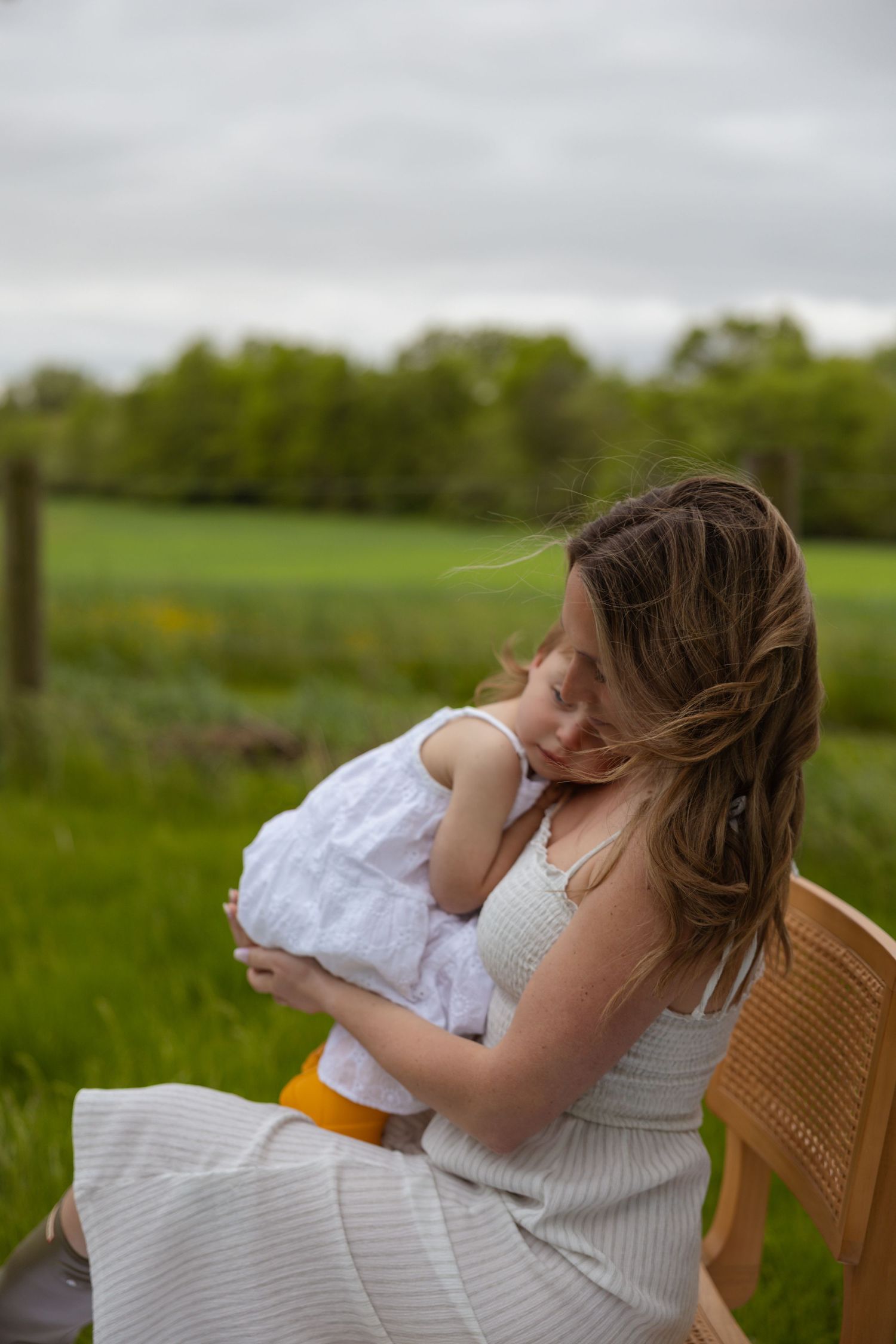 A peaceful outdoor scene showing a parent cradling a child in a wicker chair amidst green fields.