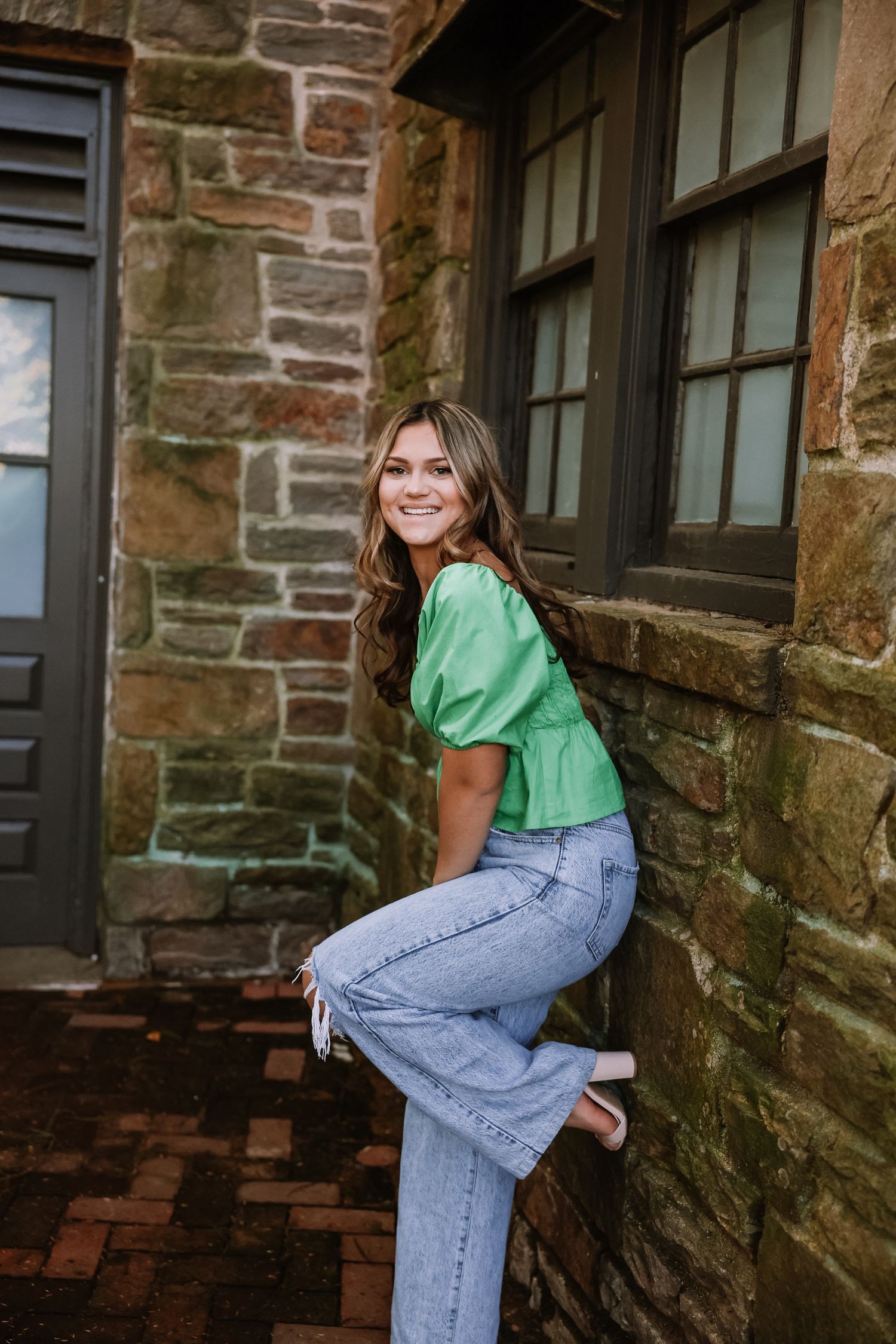 Green puff sleeve top and jeans styled against rustic stone wall architecture.