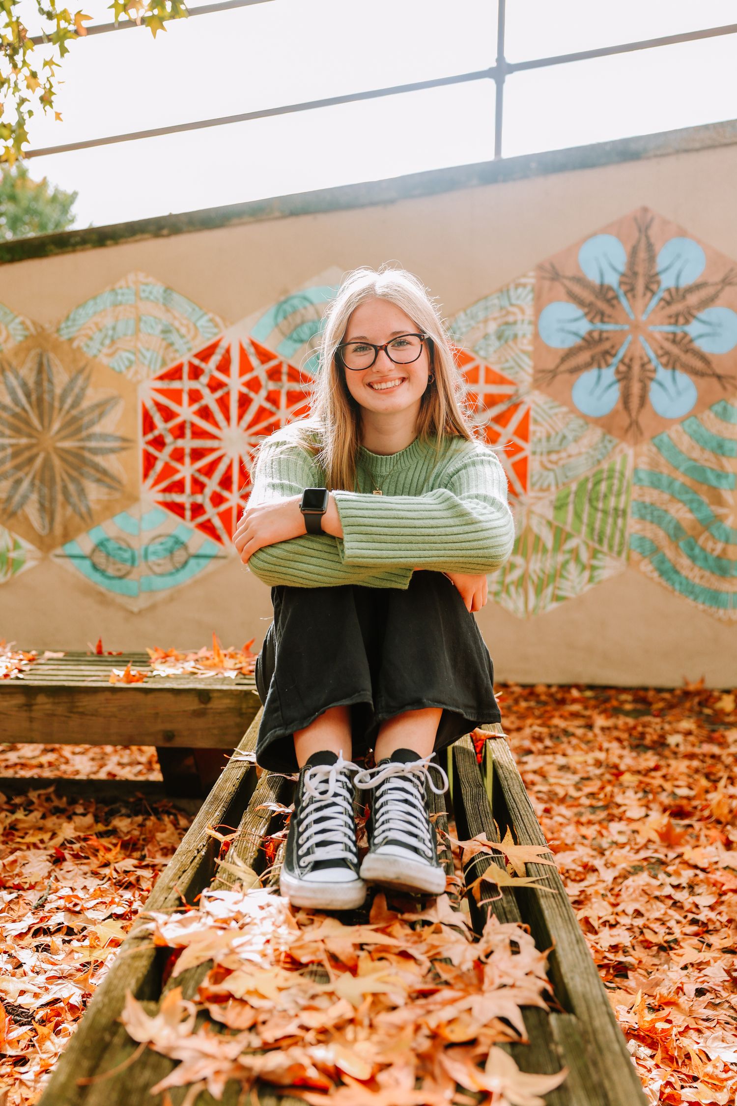 Casual autumn portrait against colorful geometric wall art with fallen leaves.