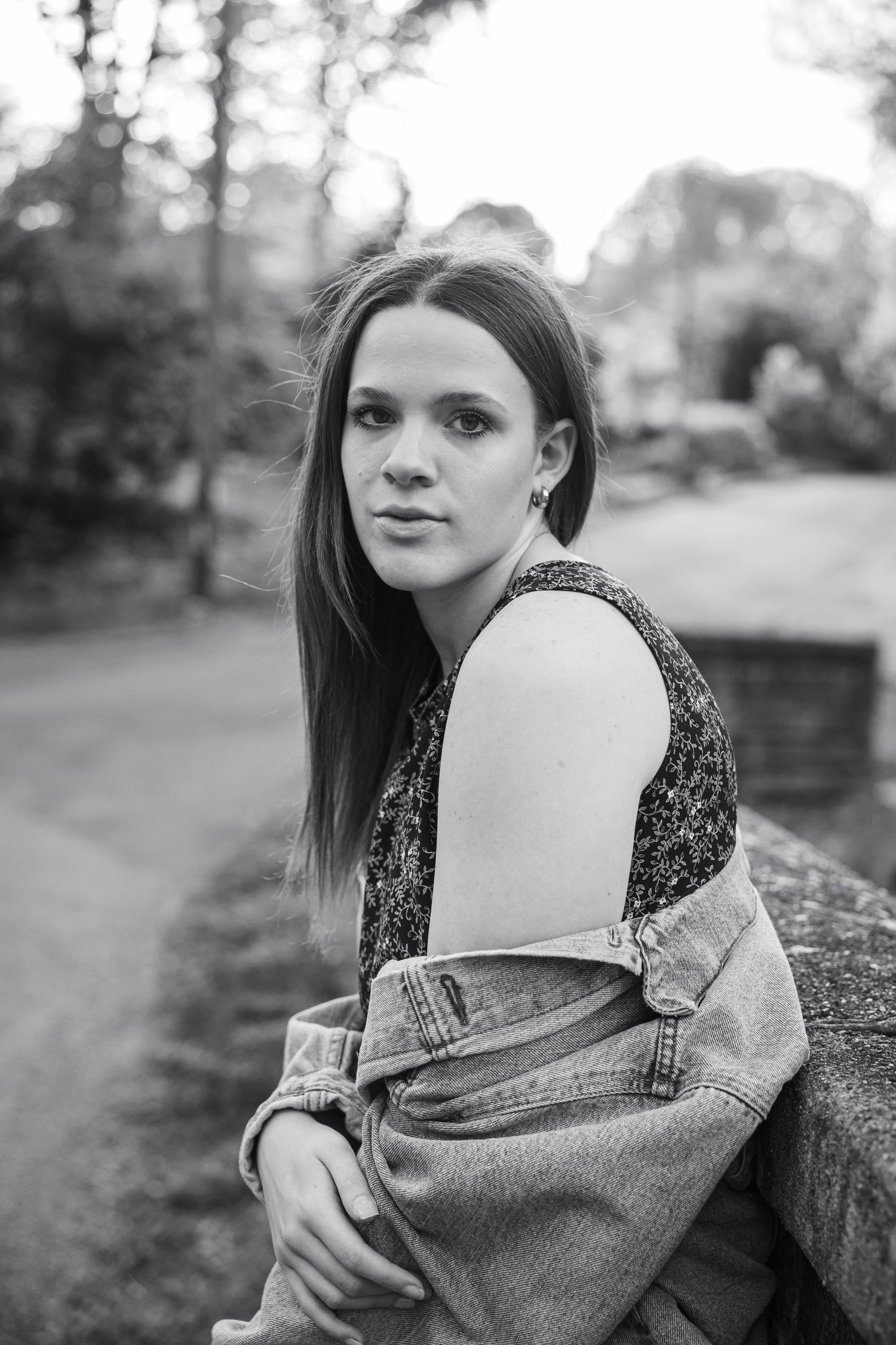 Black and white portrait of person in denim jacket leaning against stone wall outdoors.