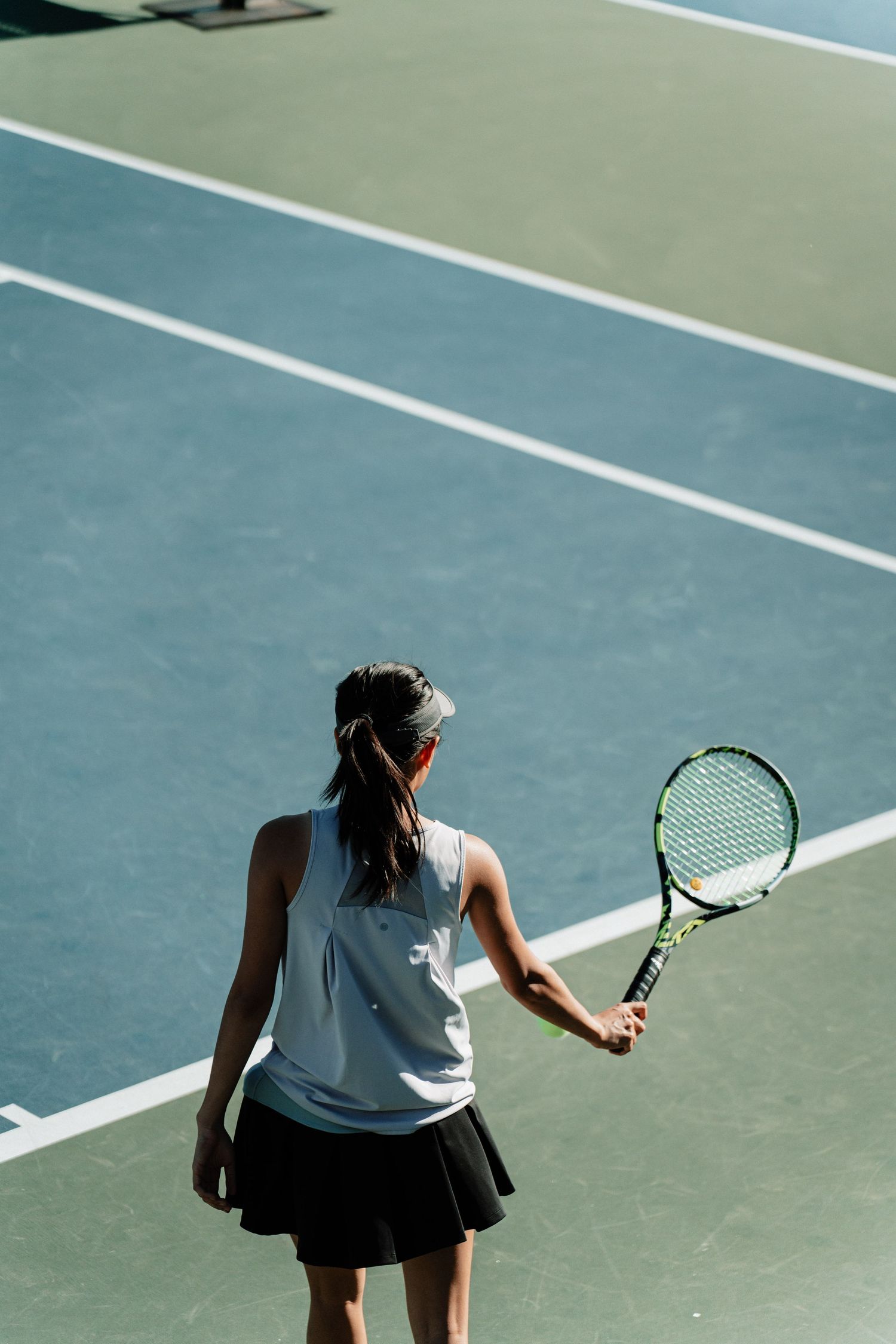 A girl bounces a tennis ball before serving.