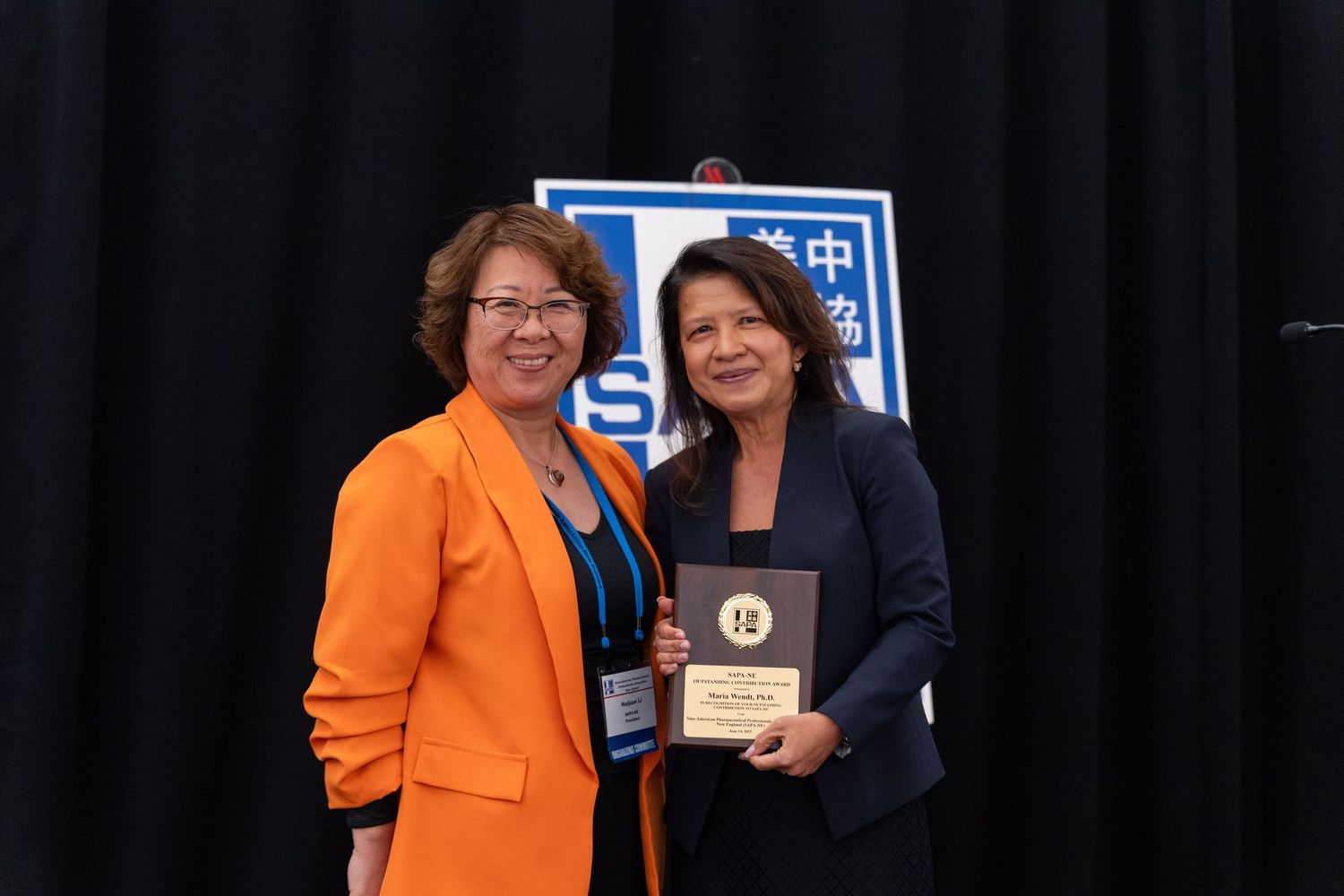 A speaker poses with an event host and her award.