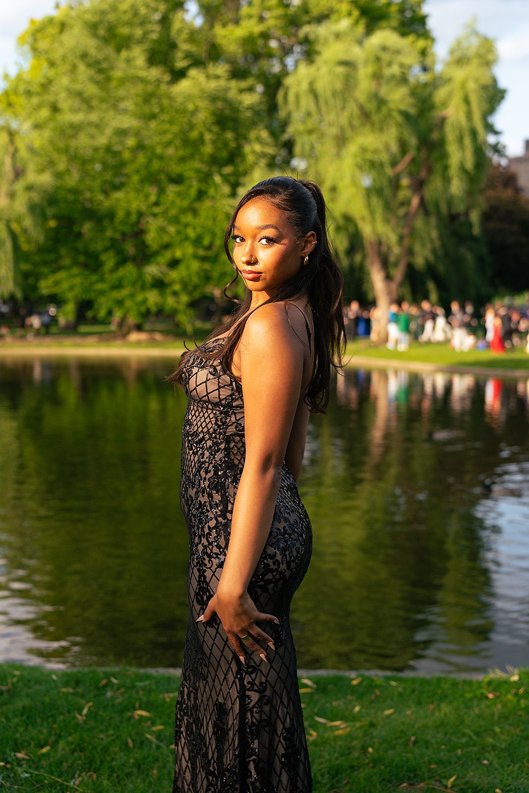 A girl poses to the left in front of the Swan Pond at Boston Public Garden
