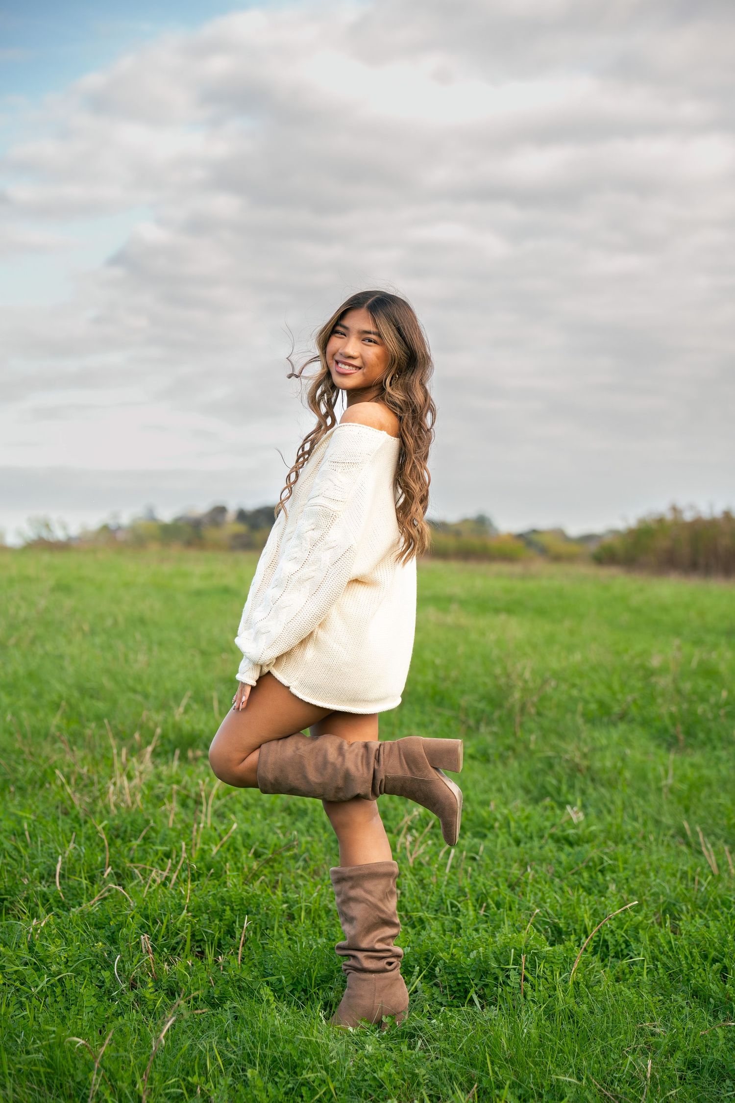 A girl poses left with her leg popped up in a field.