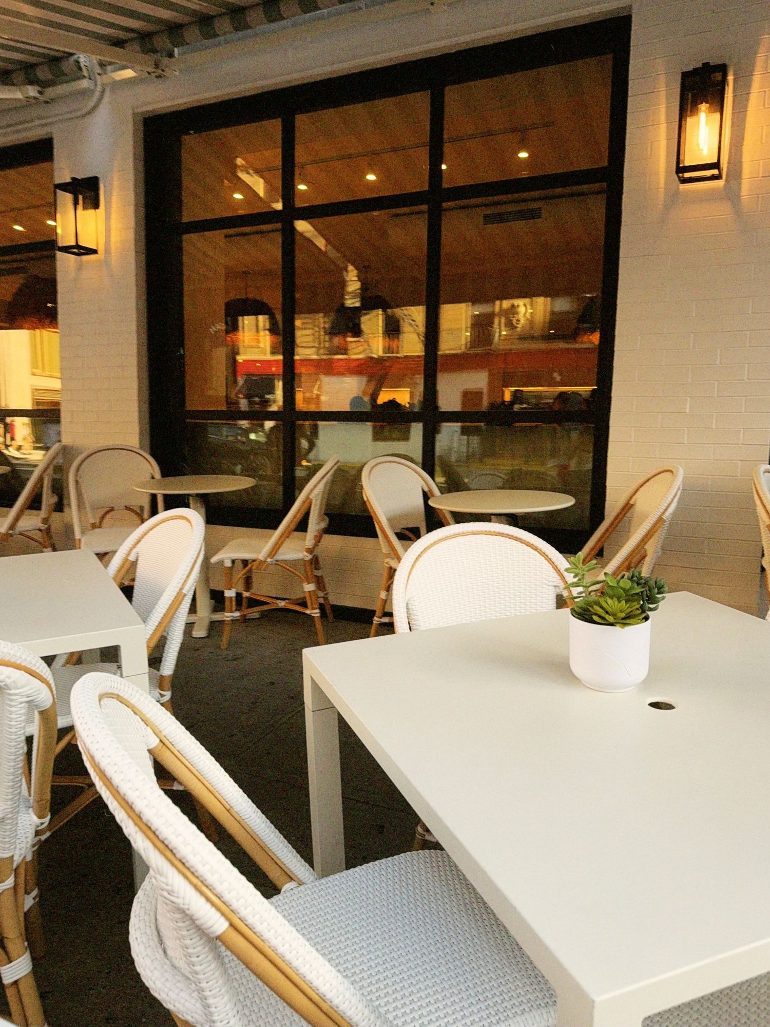 A New York City restaurant's outdoor patio seating area with white and whicker seats.