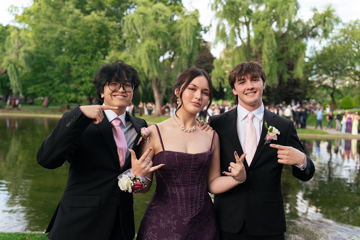 Two guys and a girl pose in front of the Swan Pond at Boston Public Garden holding a peace sign