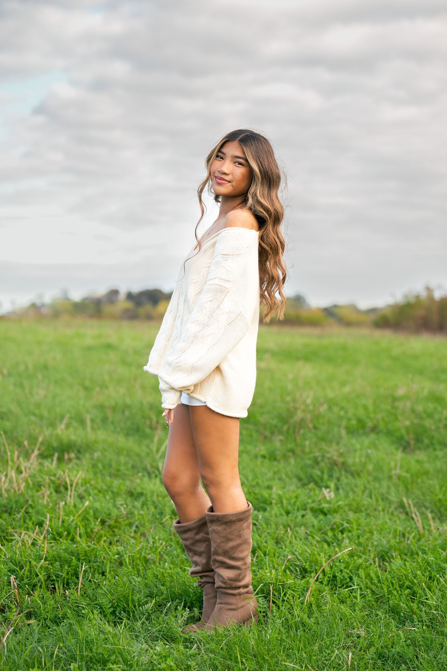 A girl poses looking to the left and facing front in a field