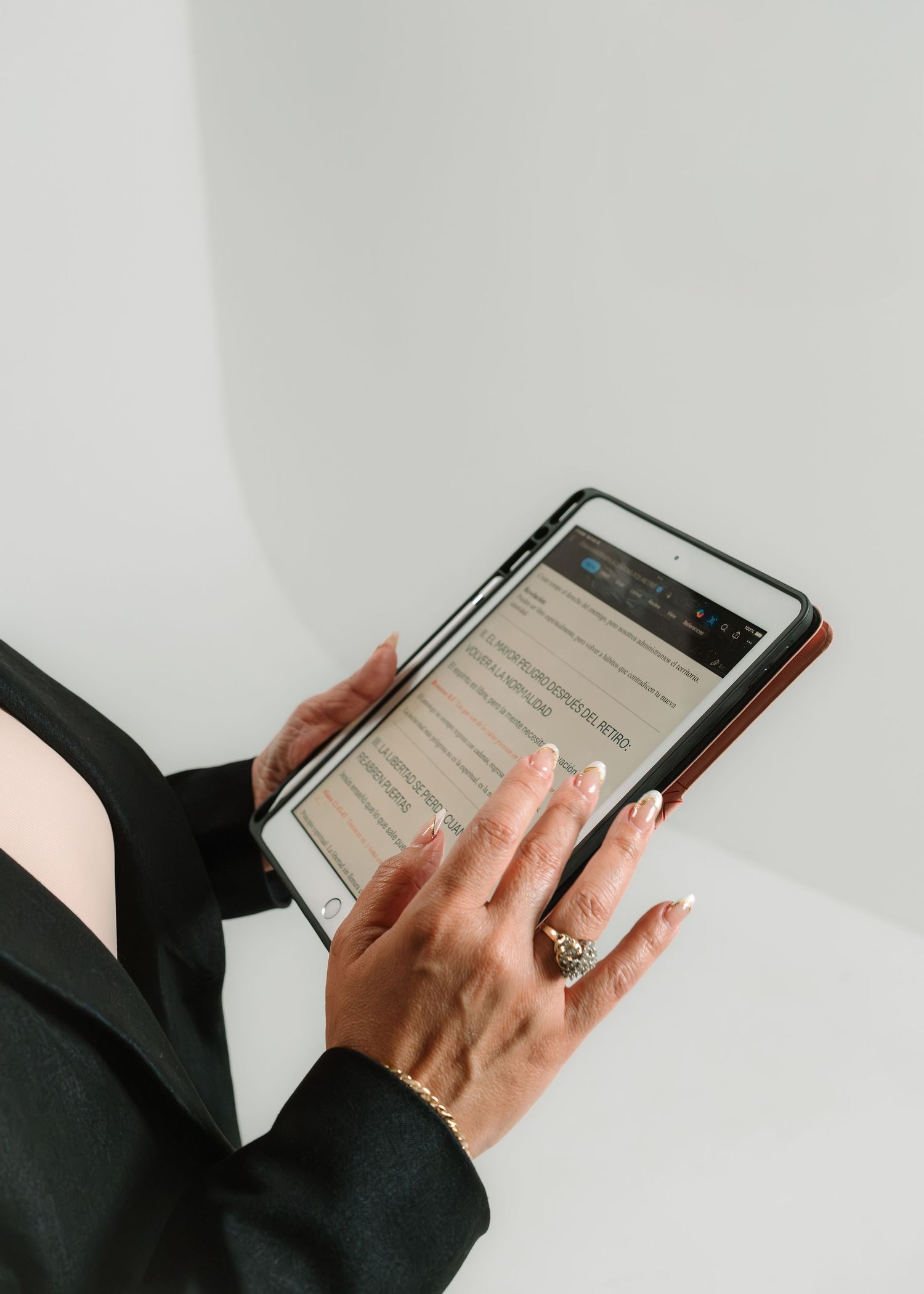Woman in black outfit holding a tablet displaying text content, wearing gold rings and bracelet.