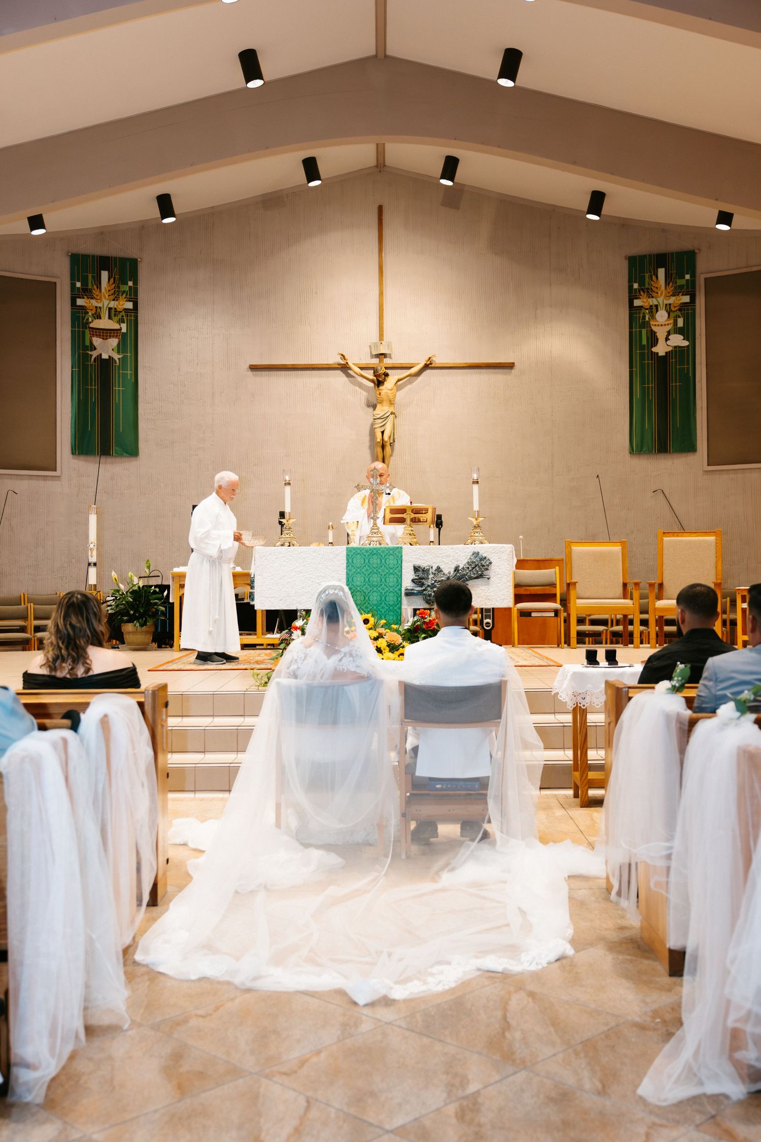 Bride and groom seated at the altar during a Catholic wedding ceremony with priests officiating at the front.