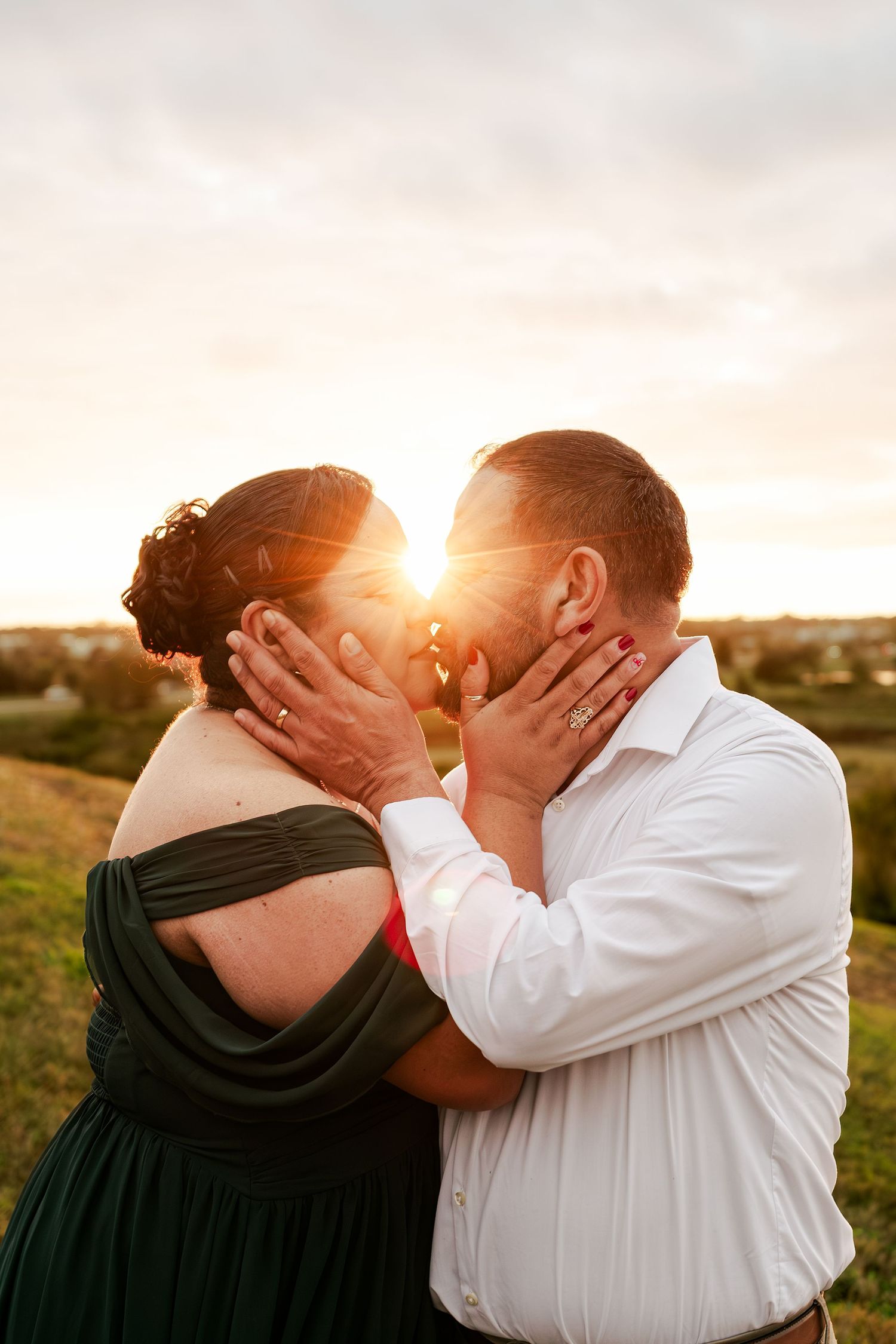 A couple shares a tender kiss at sunset in a field with golden light illuminating their silhouettes.